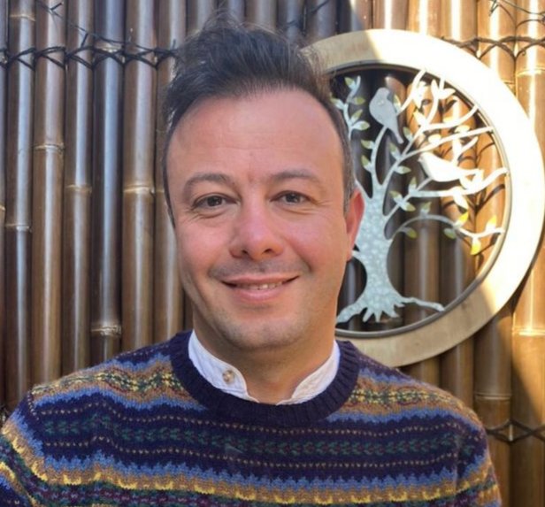 A man standing in front of a bamboo wall with a decorative tree and bird design.