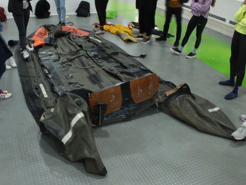 A group of people standing around and examining a large, deflated space capsule or spacecraft on the floor.