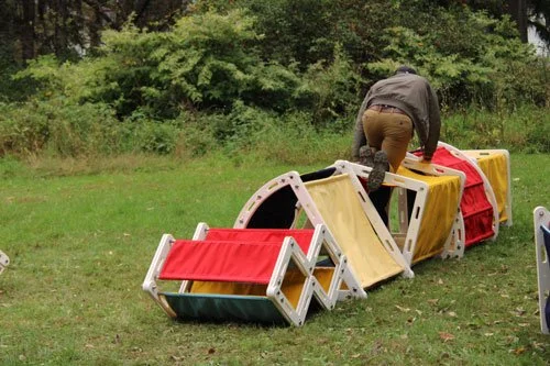 Person building a makeshift obstacle course with plastic chairs and sports equipment on grass