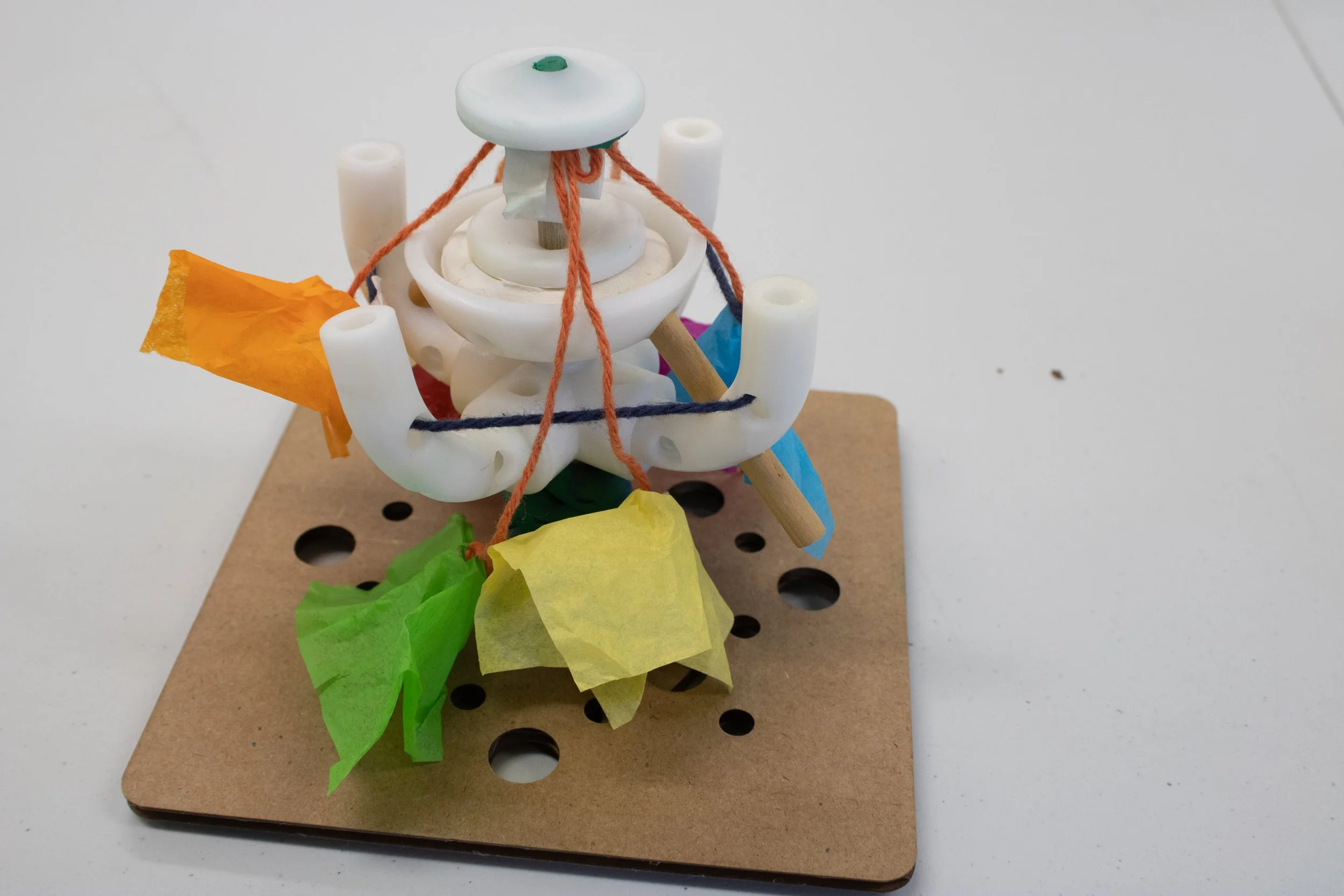 A small model of a bicycle with paper decorations attached to it, placed on a perforated cork surface.