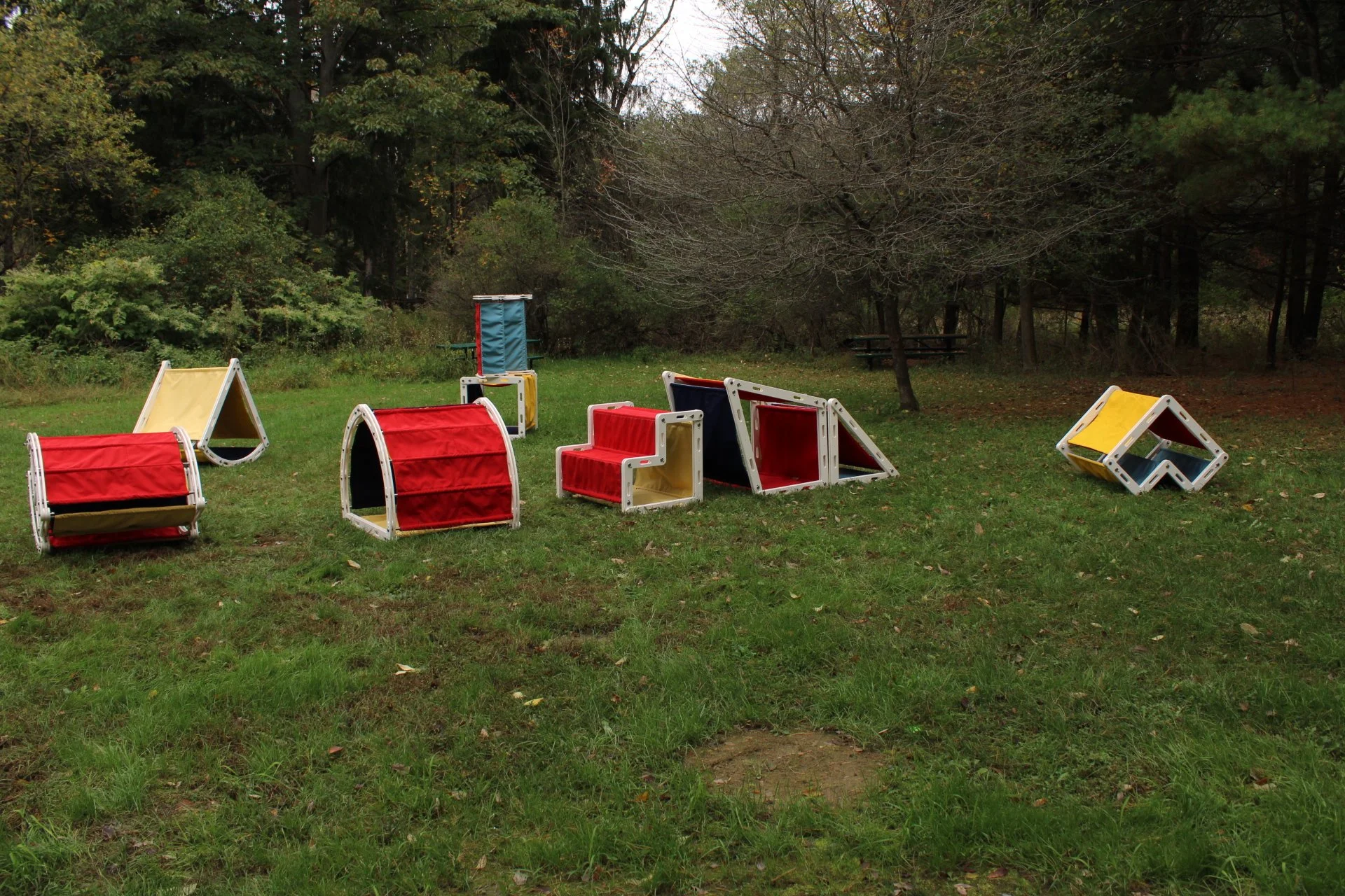 Outdoor scene with colorful modular playground equipment on grassy field surrounded by trees.