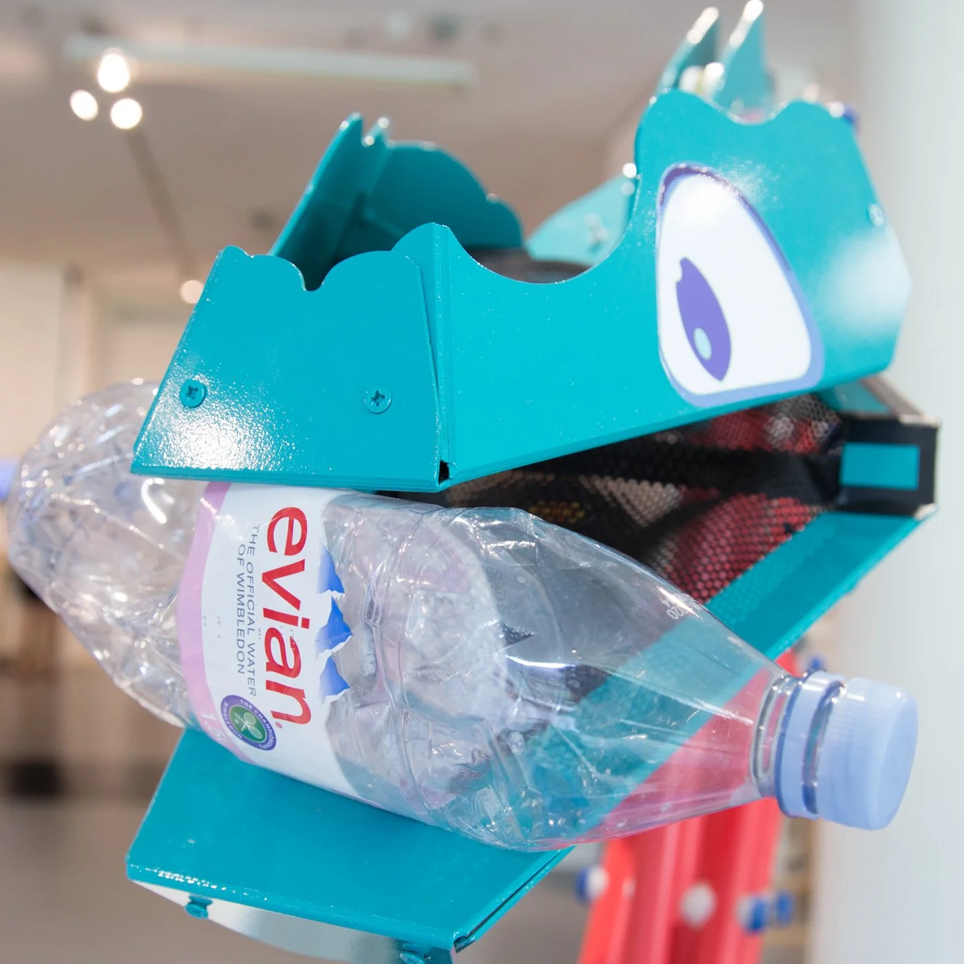 A blue bird-shaped water bottle holder with a plastic water bottle inside, placed on a teal surface.