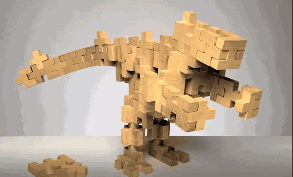 A wooden sculpture of a dinosaur, built from interlocking wooden blocks, standing on a flat surface with a light gray background.