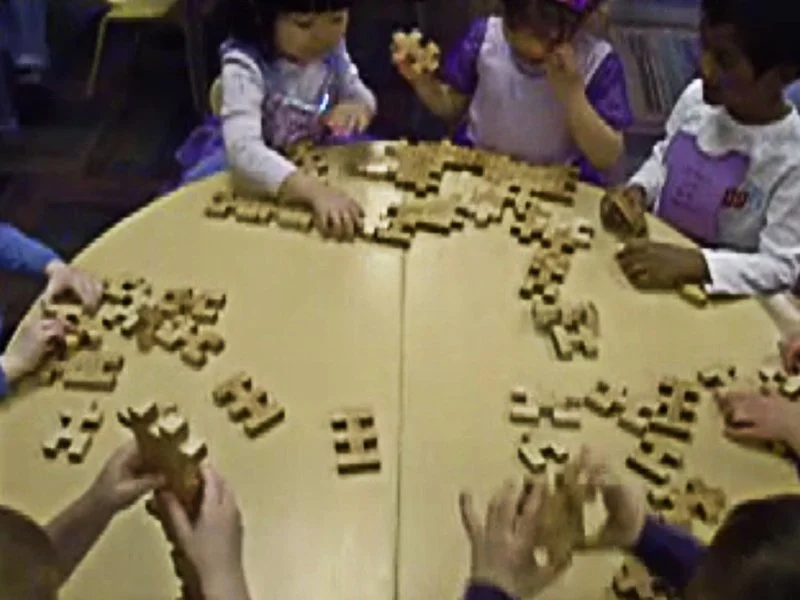 Children playing and arranging wooden blocks with patterns on a table in a classroom.