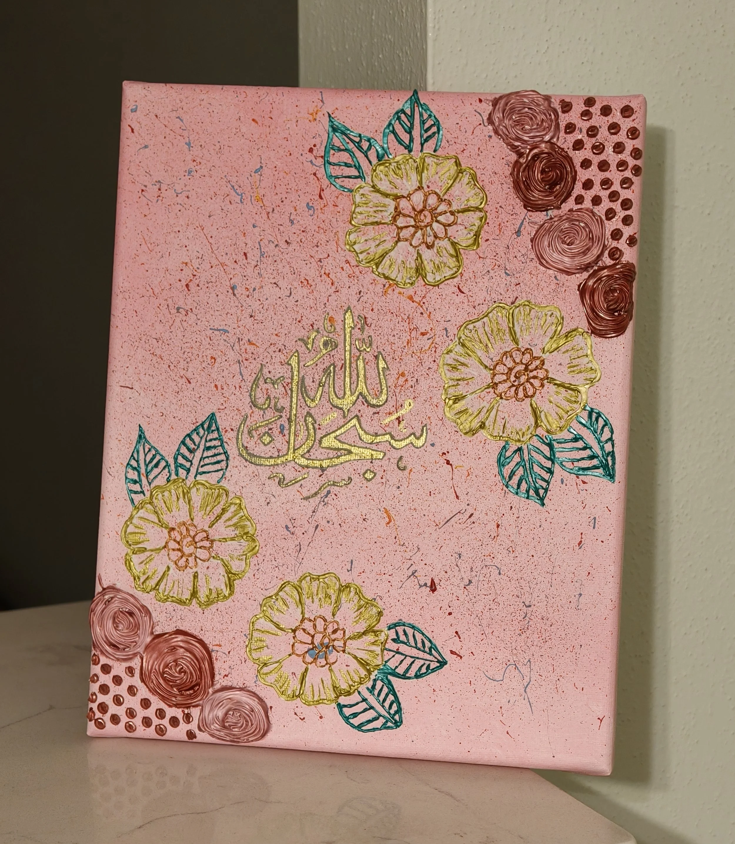 Handmade 3D Islamic calligraphy artwork featuring SubhanAllah in gold lettering, adorned with raised rose motifs and henna-inspired details on a soft pink background. Set on a white table