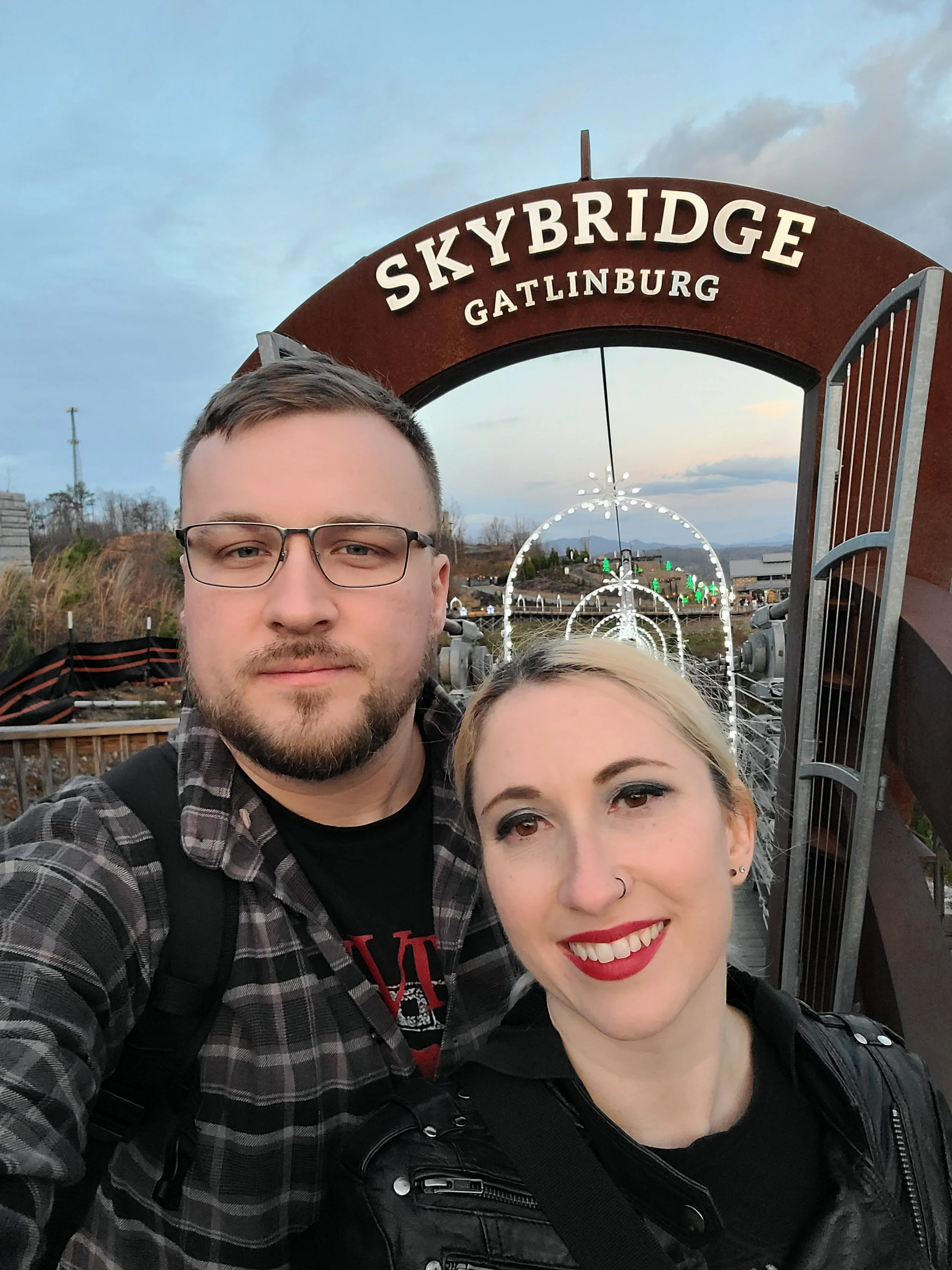 A man and a woman taking a selfie at Skybridge Gatlinburg, with the sky and decorative lights in the background.