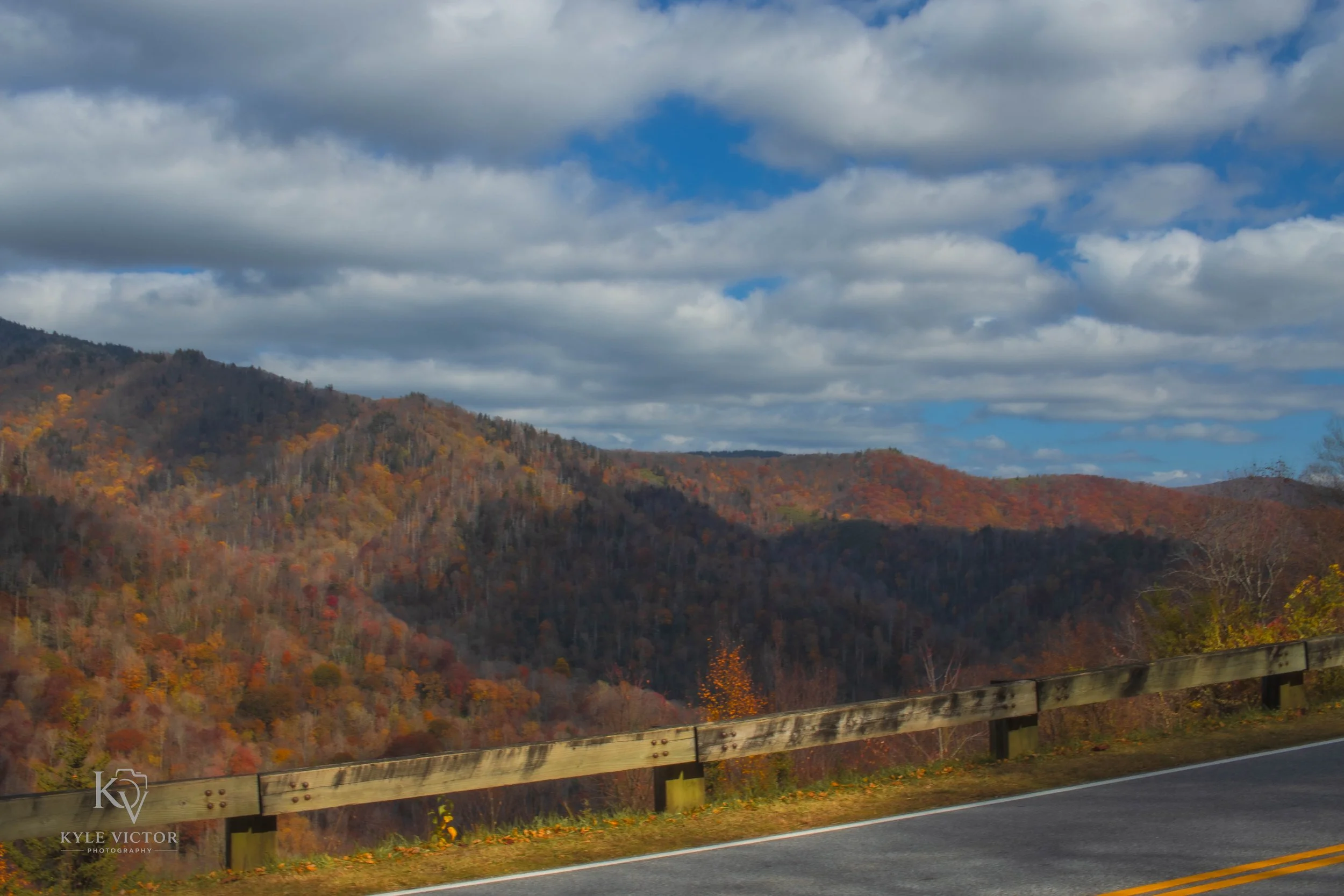 Scenic view of rolling hills covered with autumn-colored trees under a partly cloudy sky with grey and white clouds.
