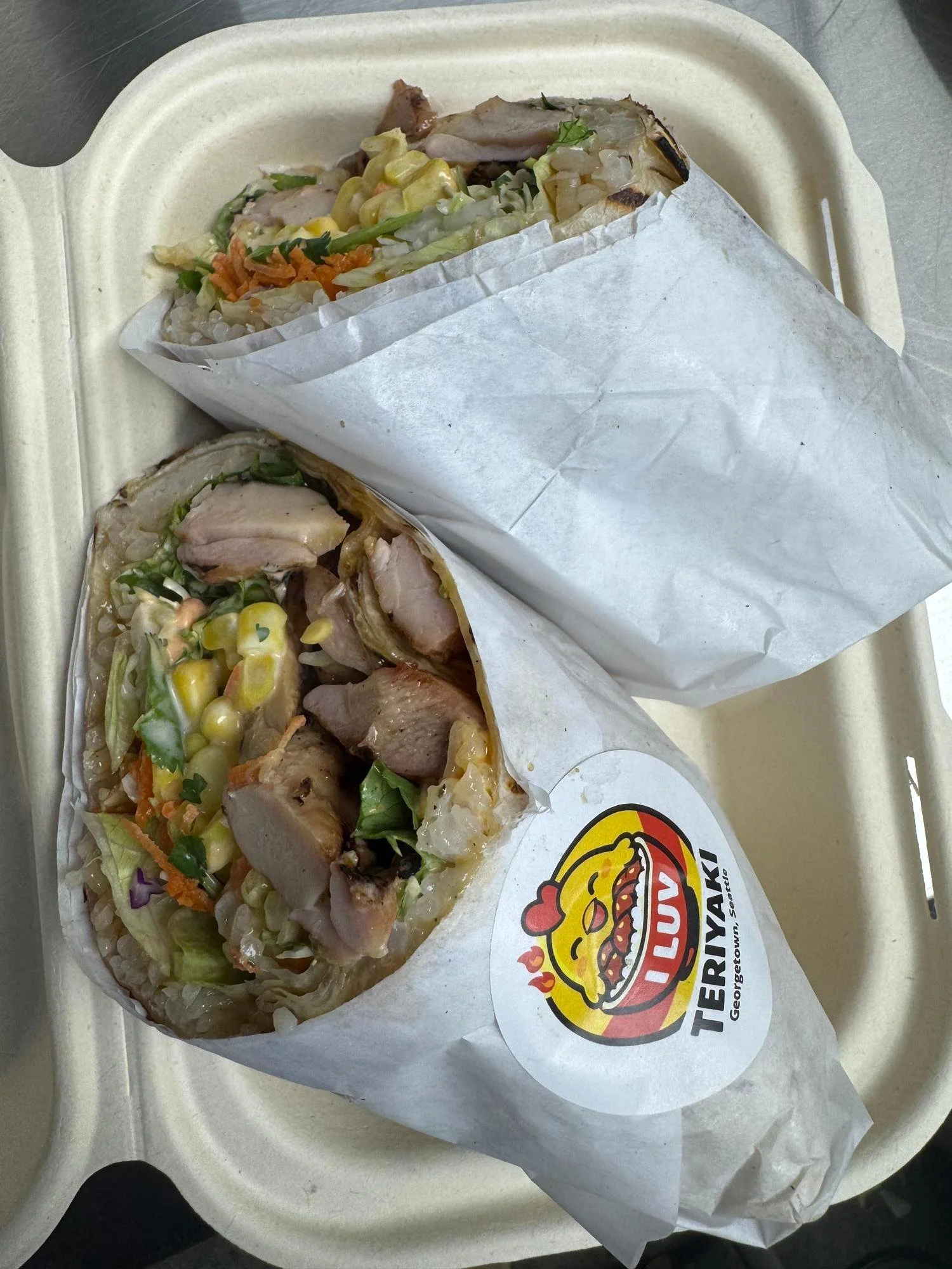 Two burritos with grilled chicken, lettuce, corn, and shredded carrots on a takeout tray