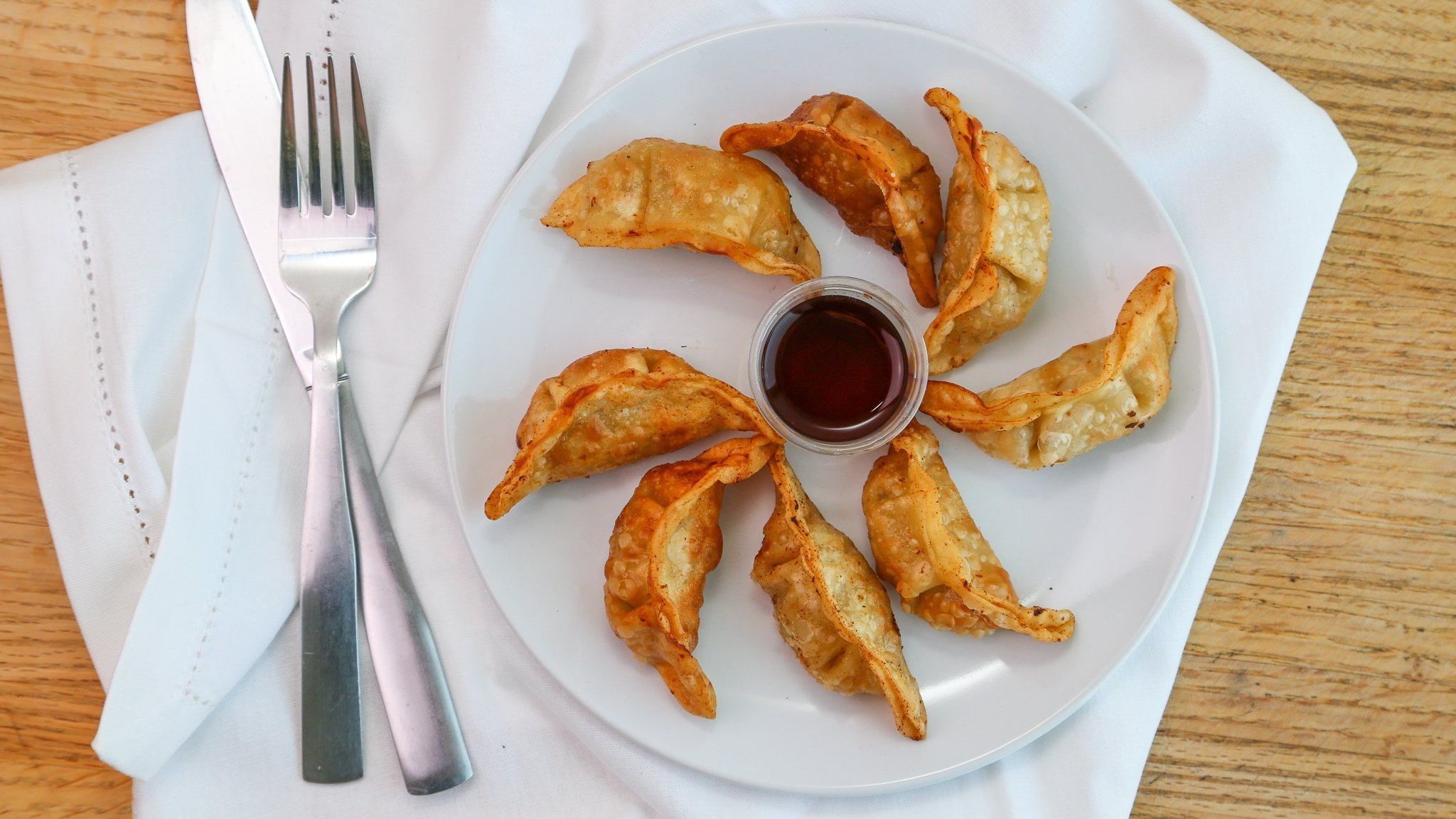 A white plate with fried dumplings and a small container of dipping sauce