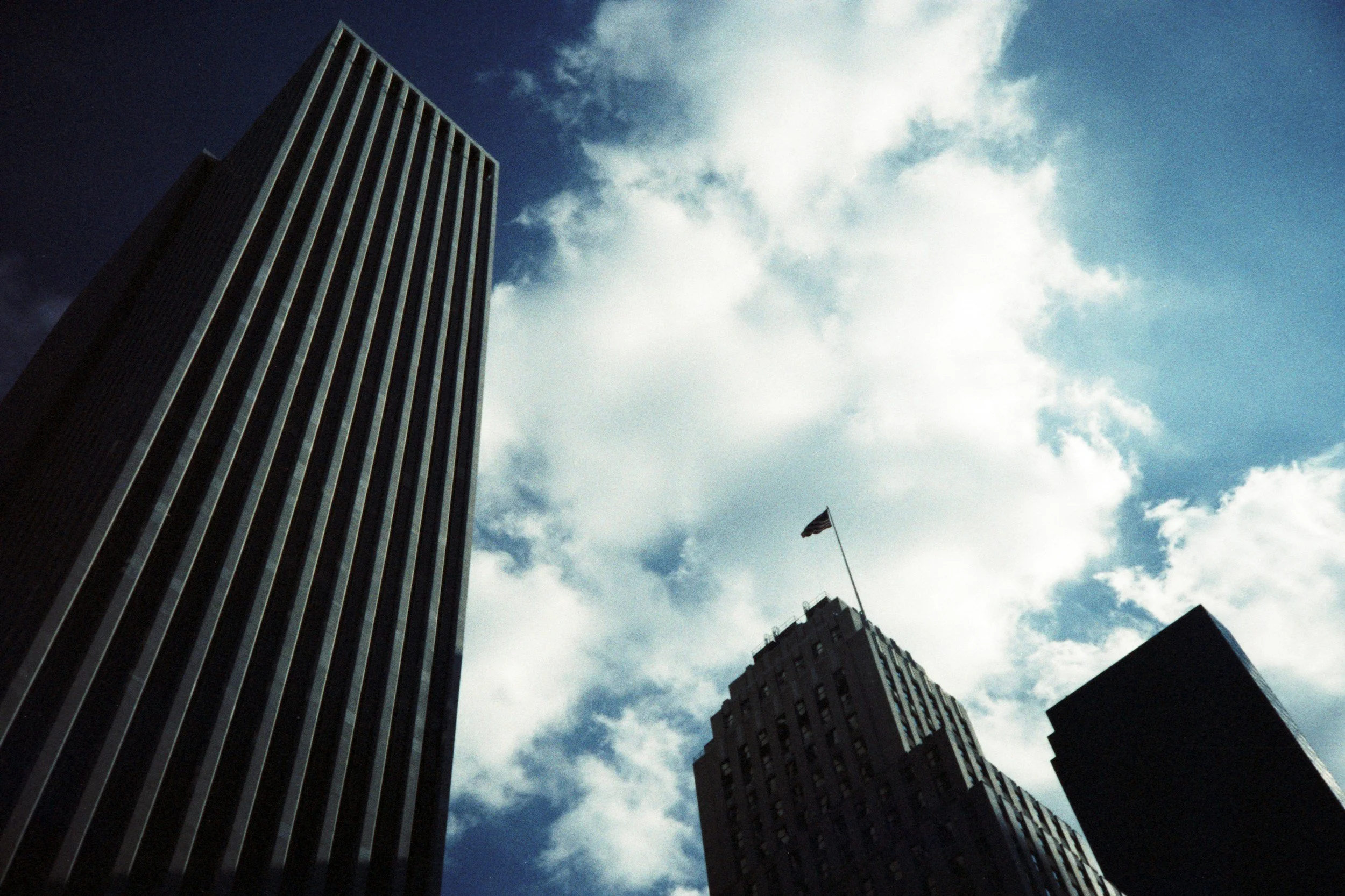 Tall skyscrapers against a partly cloudy blue sky with an American flag on one of the buildings.