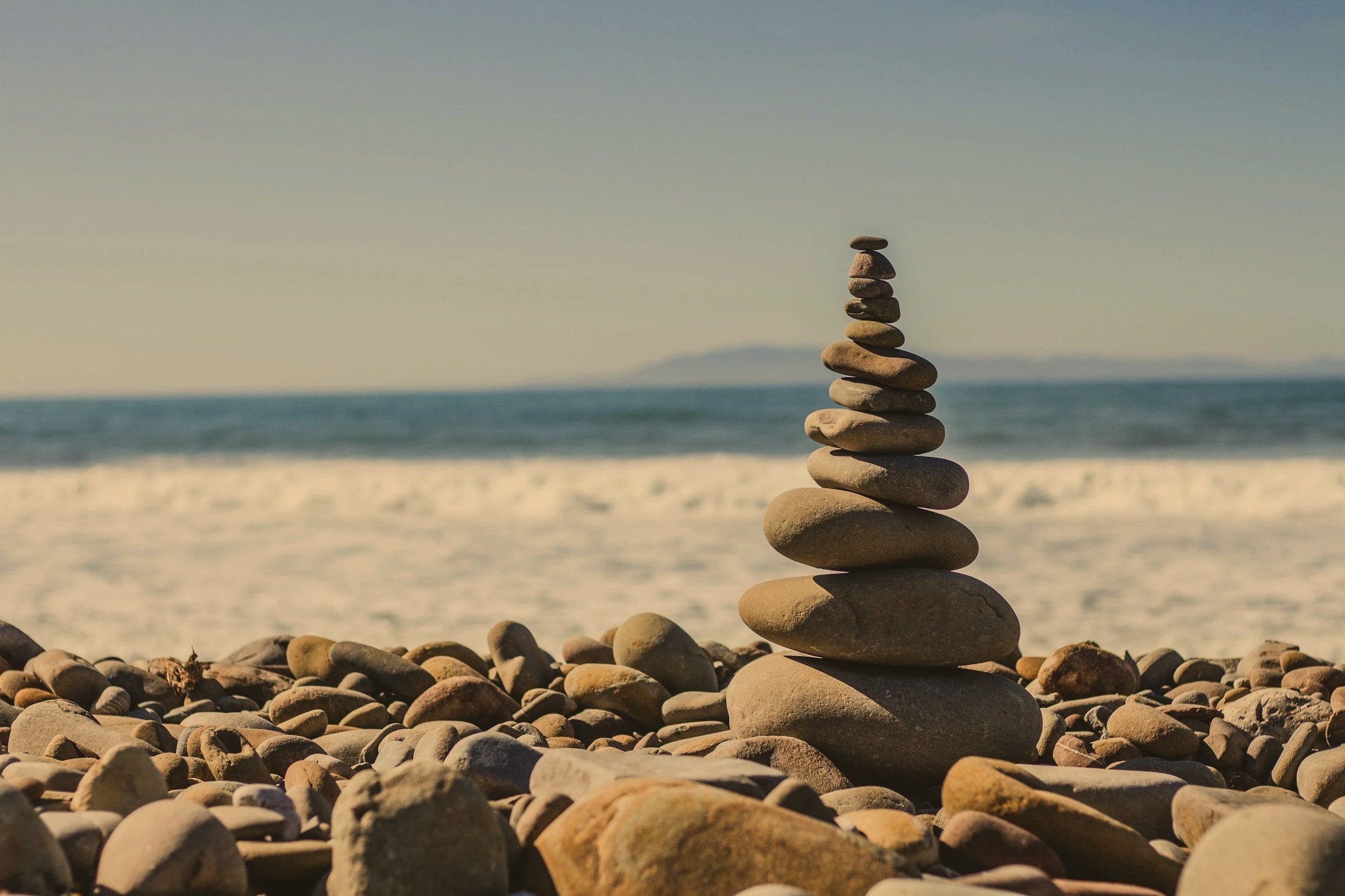 A stack of rocks balanced on top of each other on a pebbly beach, with the ocean and sky in the background.