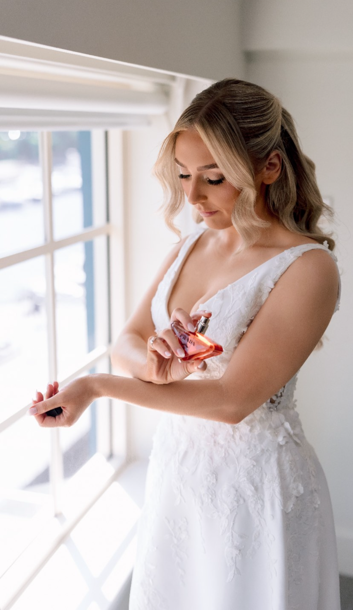 A bride in a white gown looking at a perfume bottle.