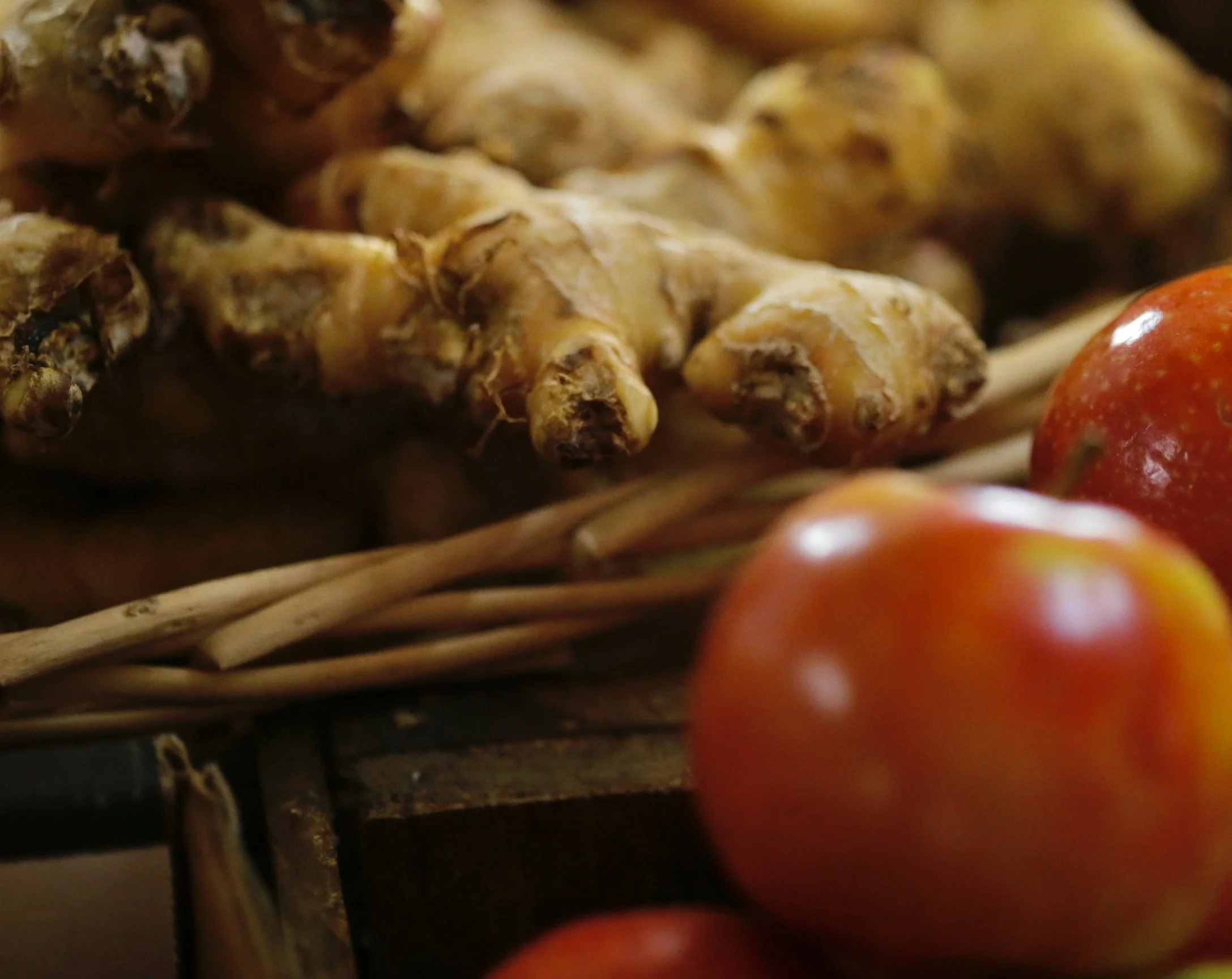Close-up of ginger roots and some red apples in a basket.