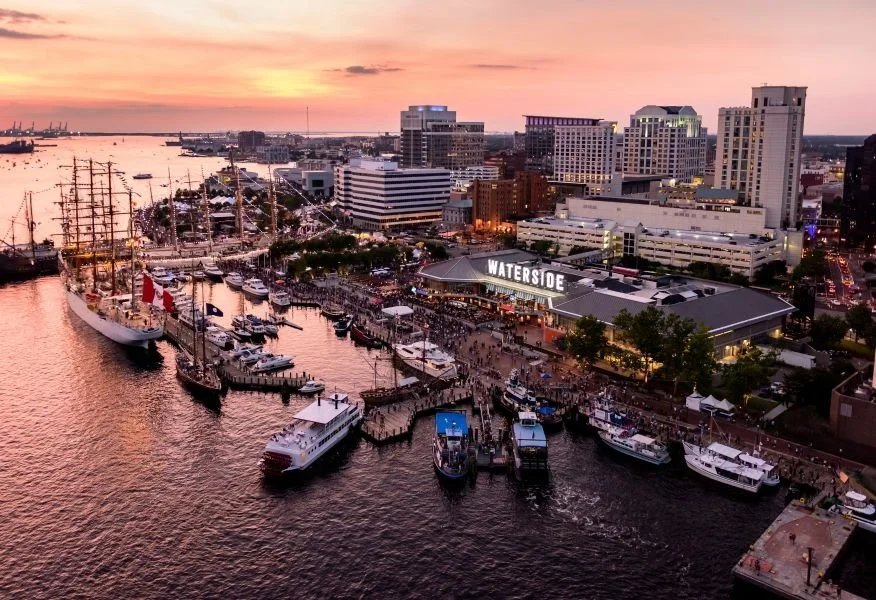 Aerial view of Baltimore Inner Harbor at sunset showing boats, high-rise buildings, and a waterfront scene with people and the Waterside area.