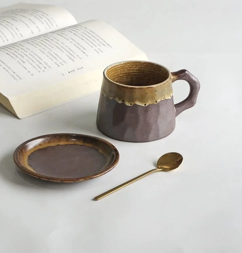 Rustic ceramic coffee mug with earthy mountain-inspired glaze, matching saucer and gold spoon — perfect for cosy coffee rituals and minimalist home café aesthetics.