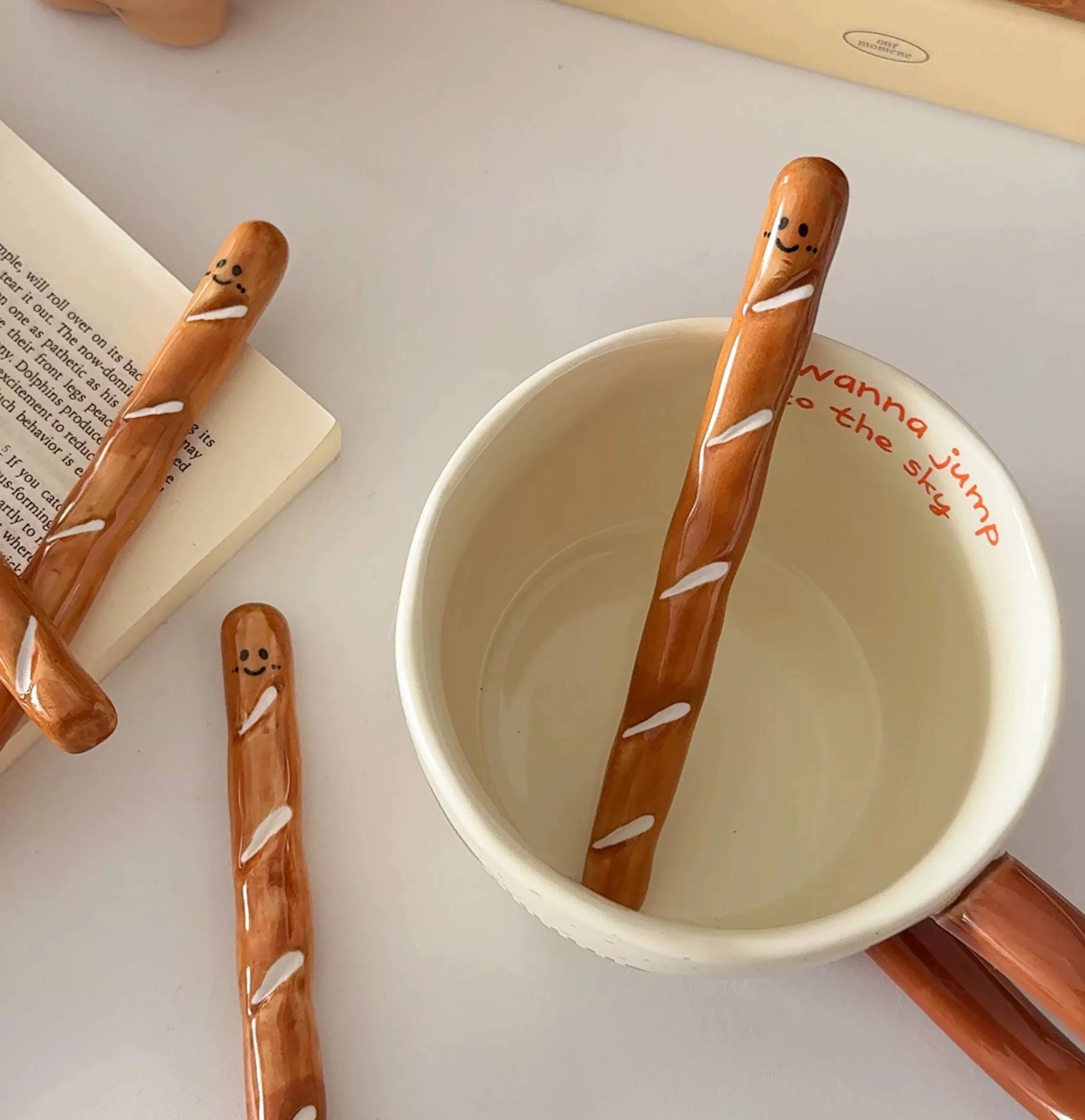 Cute baguette-shaped ceramic coffee stirrer with playful smiling face, perfect for mixing coffee, matcha and adding cosy bakery-inspired charm to your café setup.