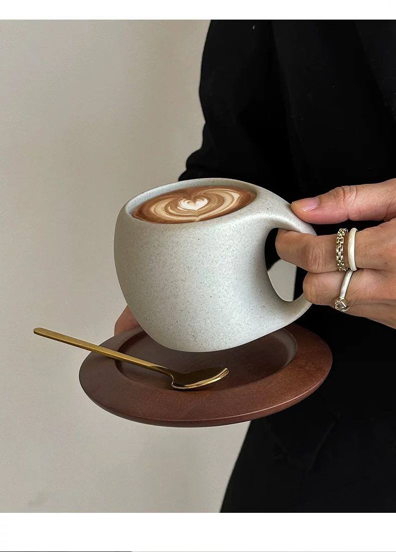 Minimalist ceramic latte mug with wooden saucer and gold spoon for cosy modern home café aesthetics.