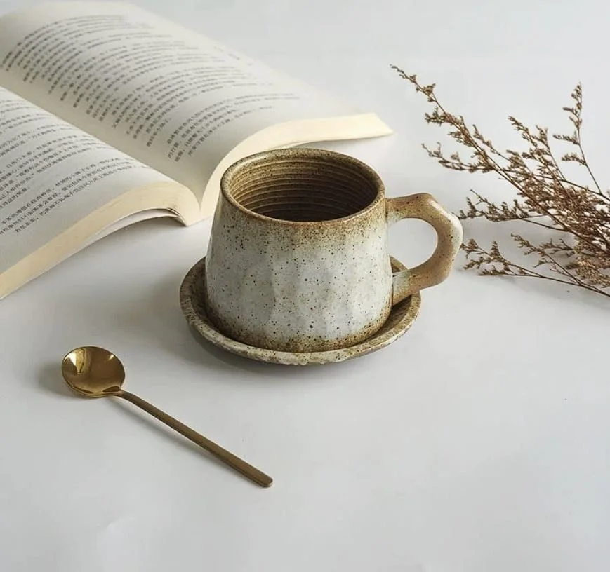 Rustic ceramic coffee mug with earthy mountain-inspired glaze, matching saucer and gold spoon — perfect for cosy coffee rituals and minimalist home café aesthetics.