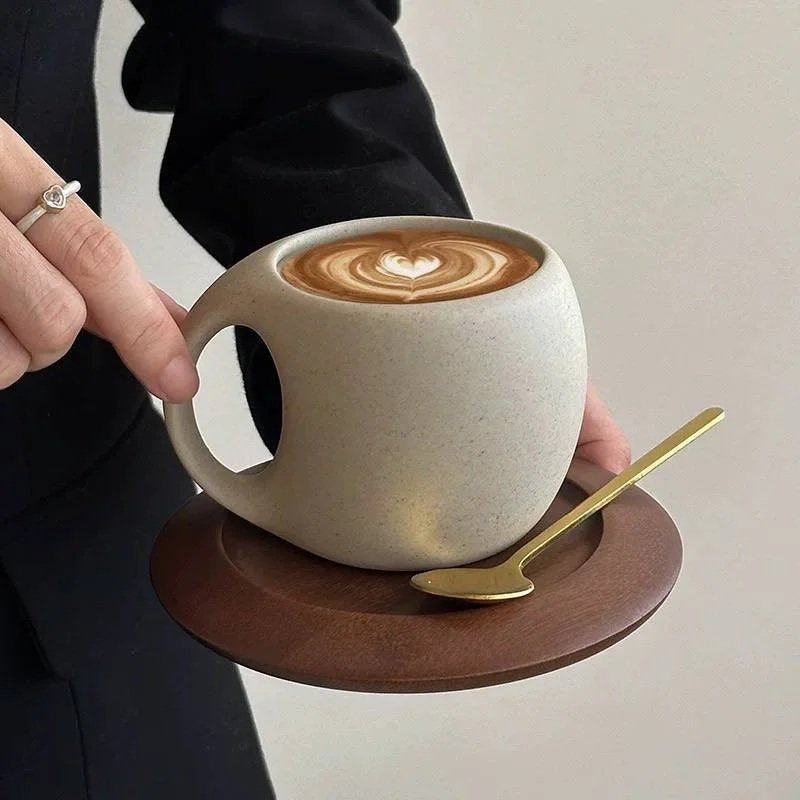Minimalist ceramic latte mug with wooden saucer and gold spoon for cosy modern home café aesthetics.