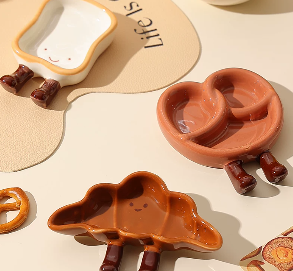 Cute pretzel, toast and croissant shaped ceramic snack plates with playful dangling legs, perfect for desserts, dipping sauces and cosy kawaii kitchen décor.
