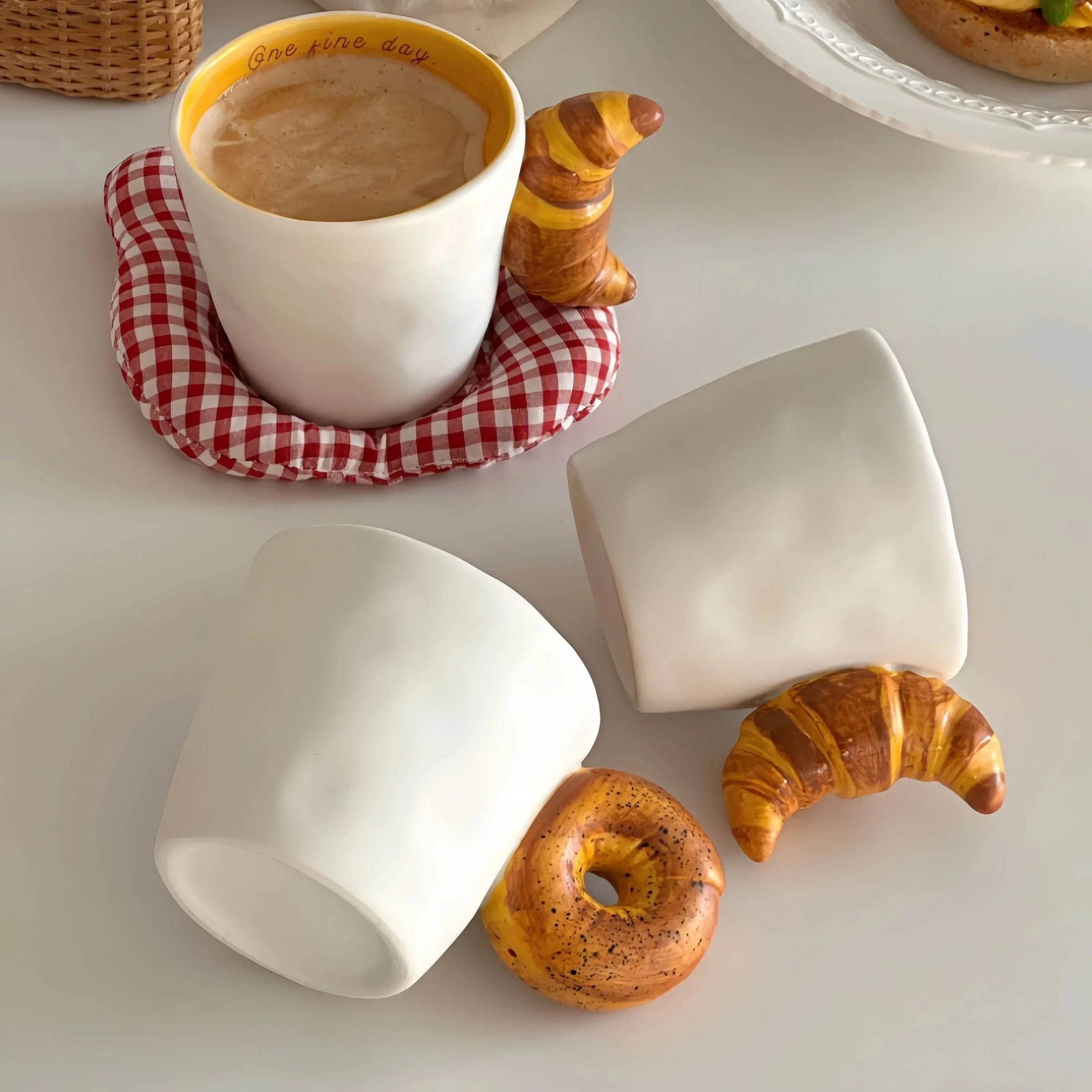 Cute ceramic mugs with croissant and bagel-shaped handles, featuring warm buttery tones and playful bakery-inspired design for cosy coffee moments.