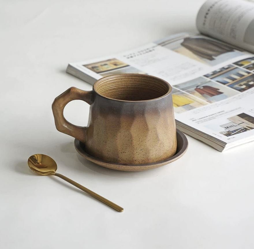 Rustic ceramic coffee mug with earthy mountain-inspired glaze, matching saucer and gold spoon — perfect for cosy coffee rituals and minimalist home café aesthetics.