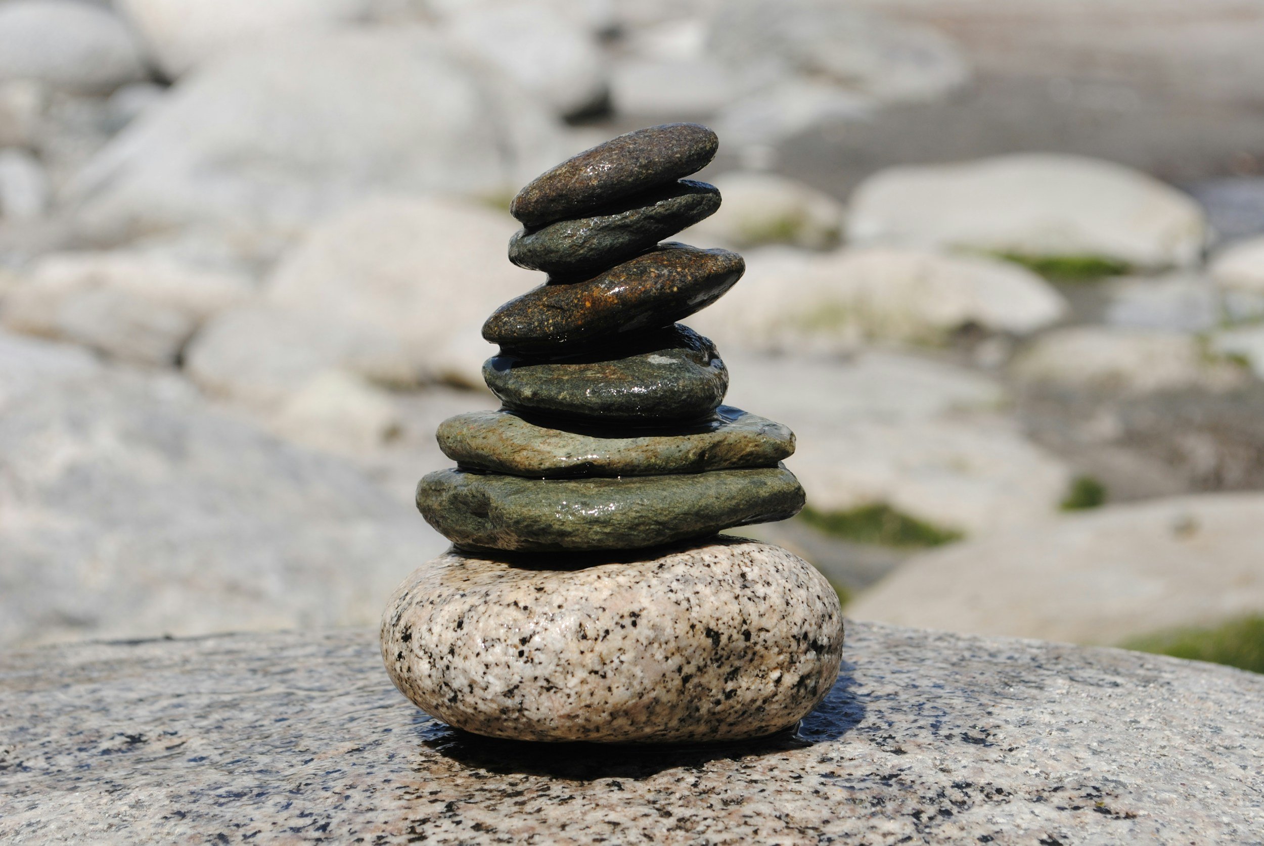 Stack of seven smooth rocks, with the largest at the bottom and the smallest at the top, on a granite surface with blurred stones in the background.