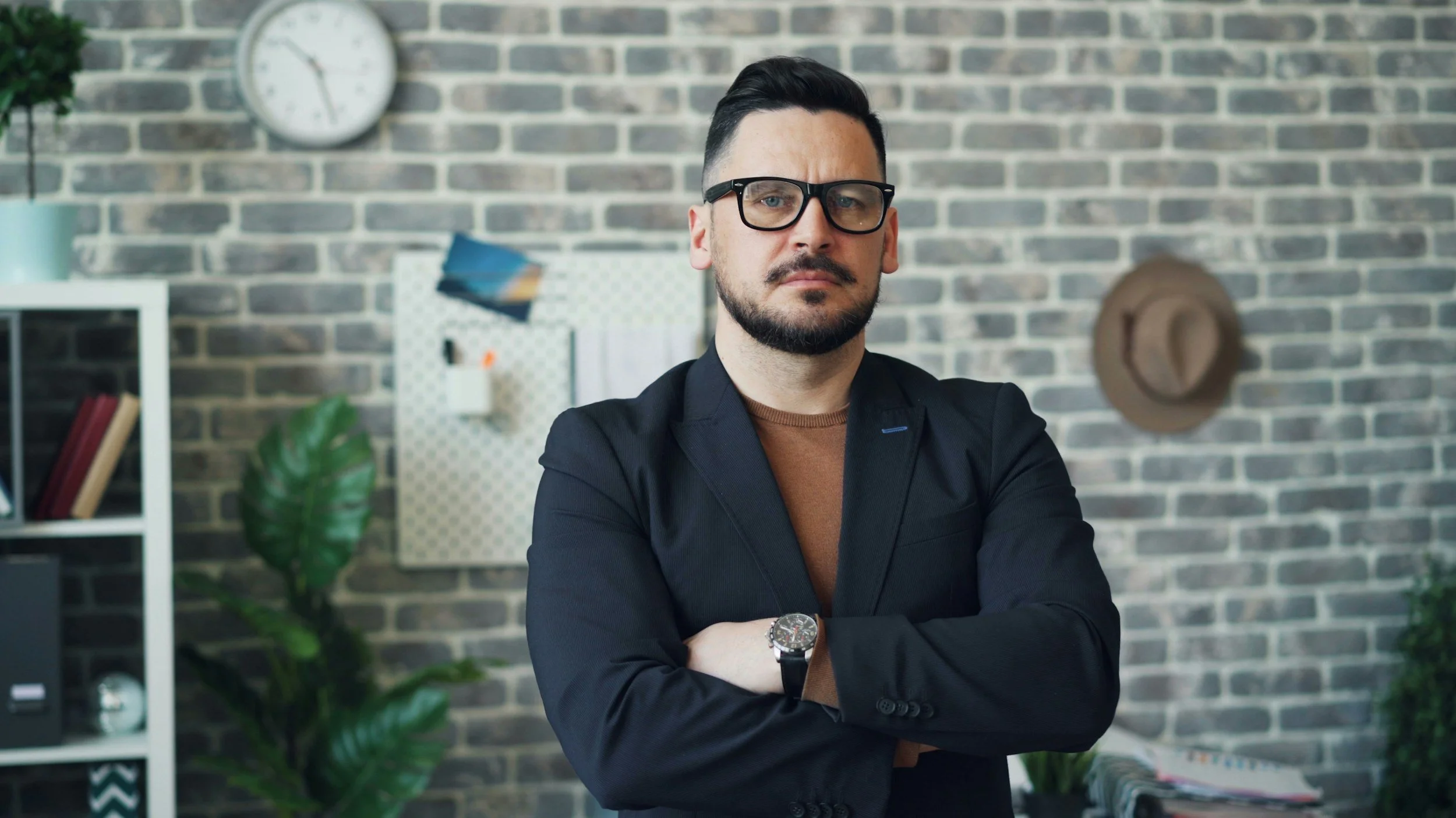 Stock photo of a man with arms crossed in front of a brick wall, representing the 'Regulated to Lead' leadership workshop.