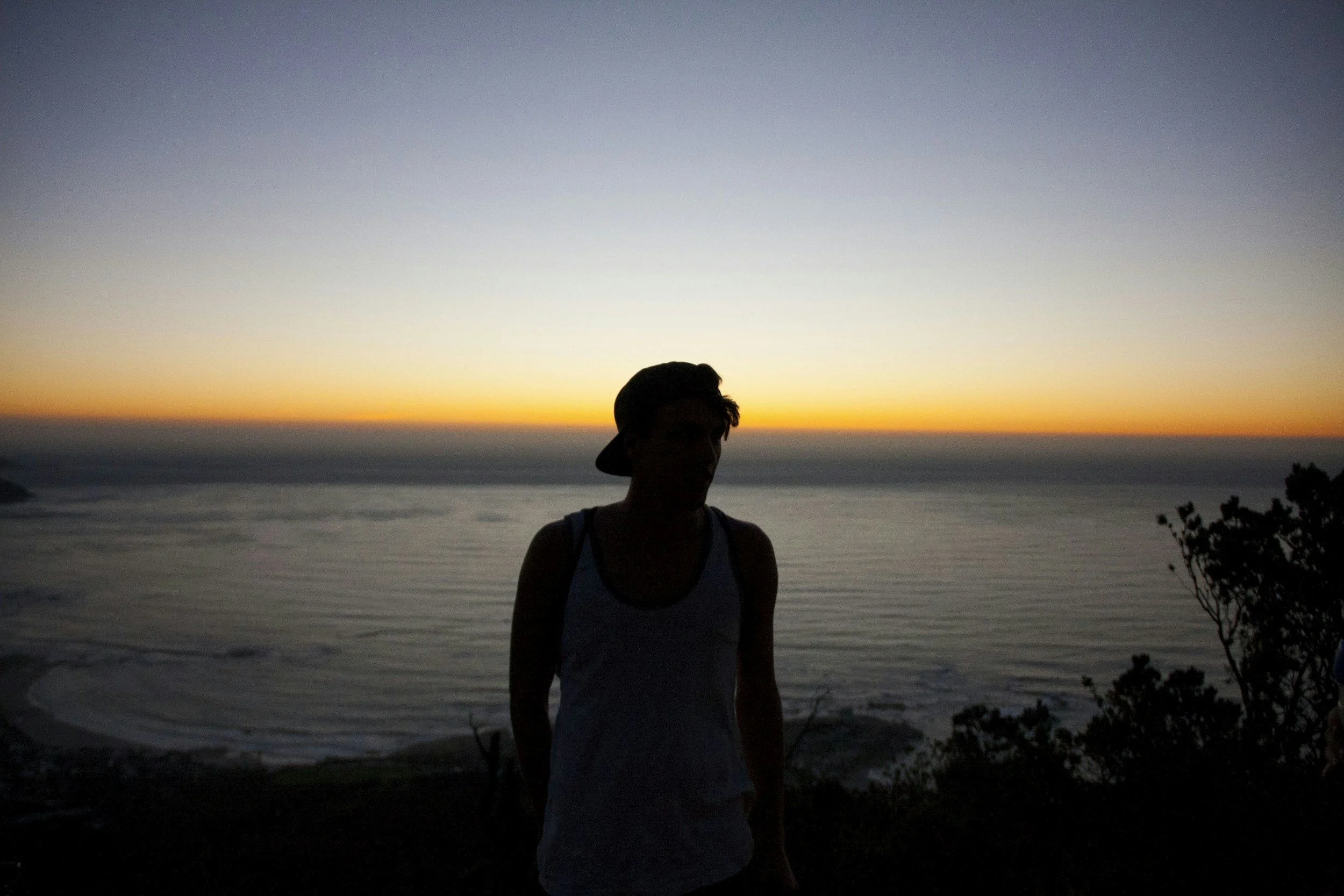 Silhouette of a person standing by the water during a sunset, with the sky transitioning from orange to blue.