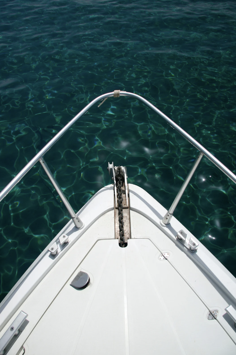 View from the bow of a boat on clear blue water, with a metal railing and anchor chain.