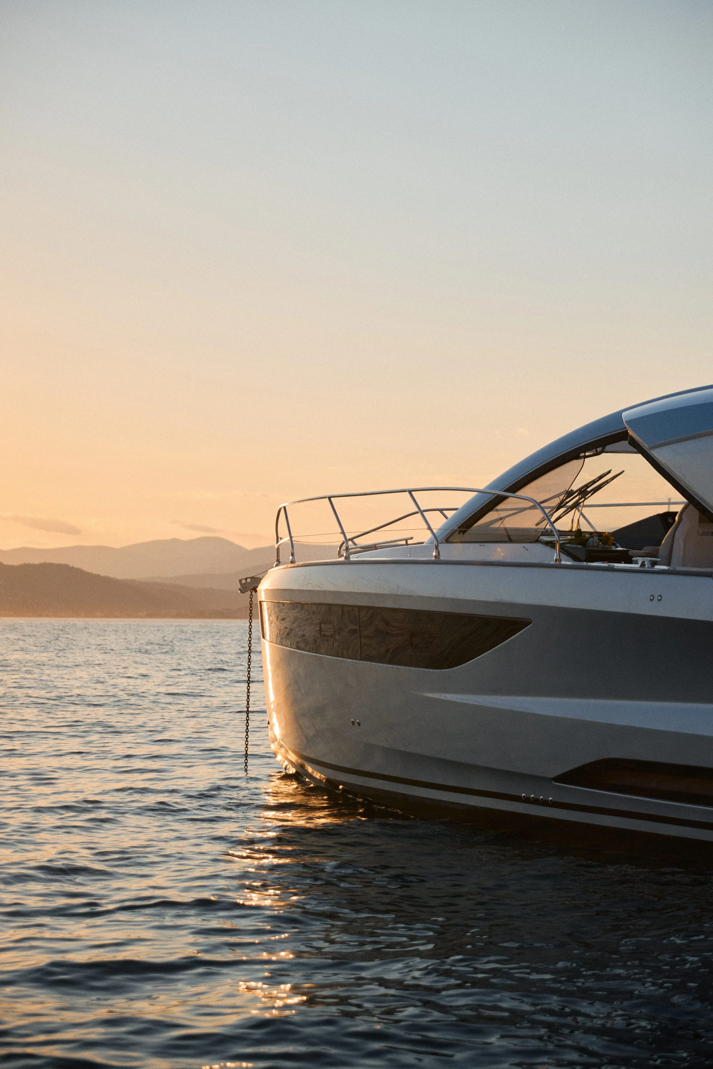 Side view of a yacht anchored in calm waters during sunset, with mountains in the background.