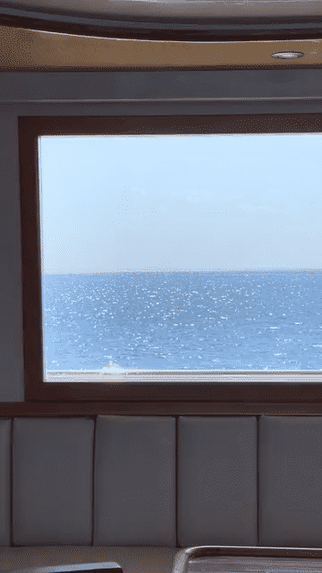 Ocean view through a boat window with sunlight reflecting on the water.