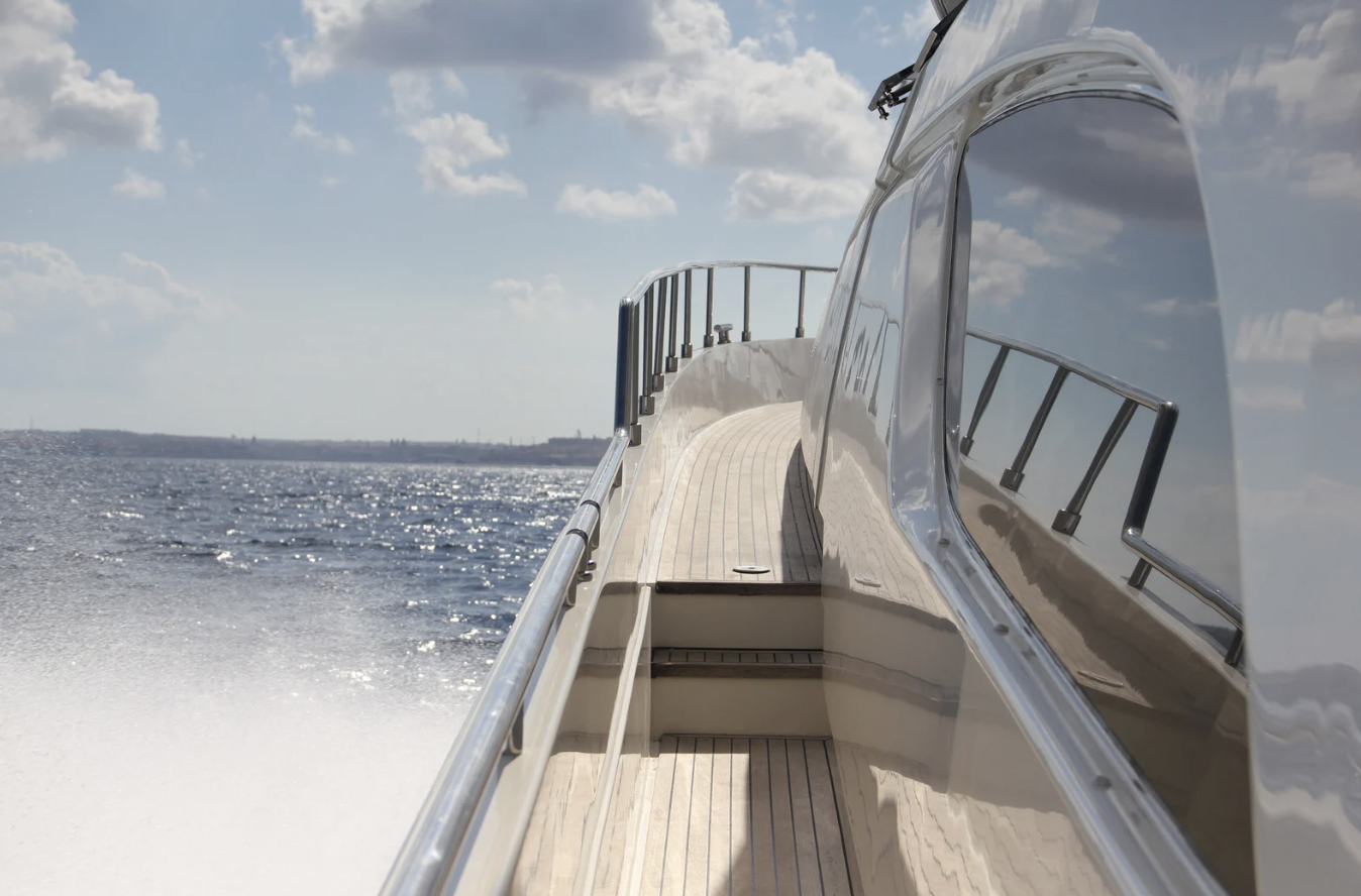 View from a yacht's deck with railings, looking out over the water on a sunny day with scattered clouds.