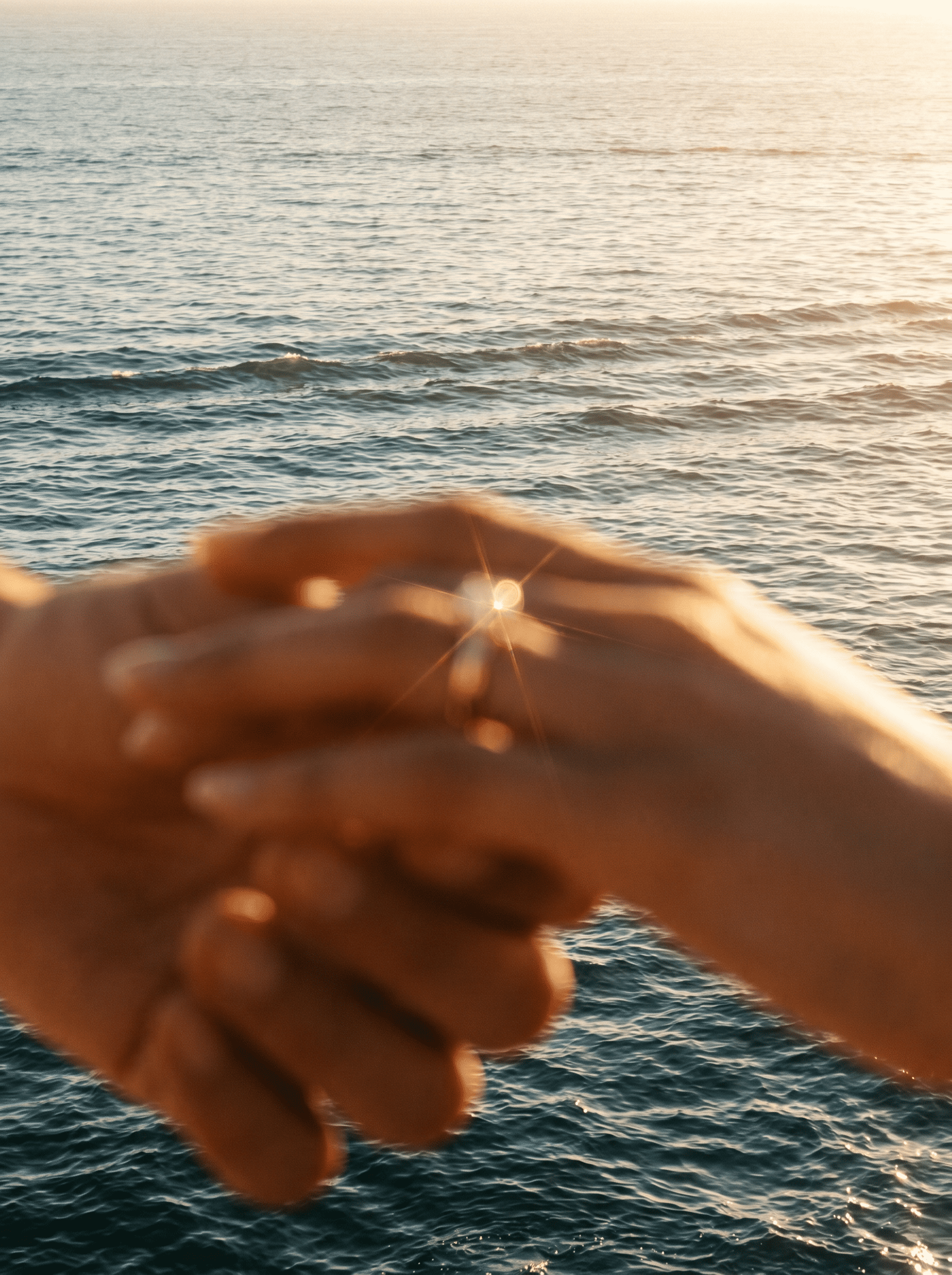 A hand holding a small object in front of an ocean and sunset.