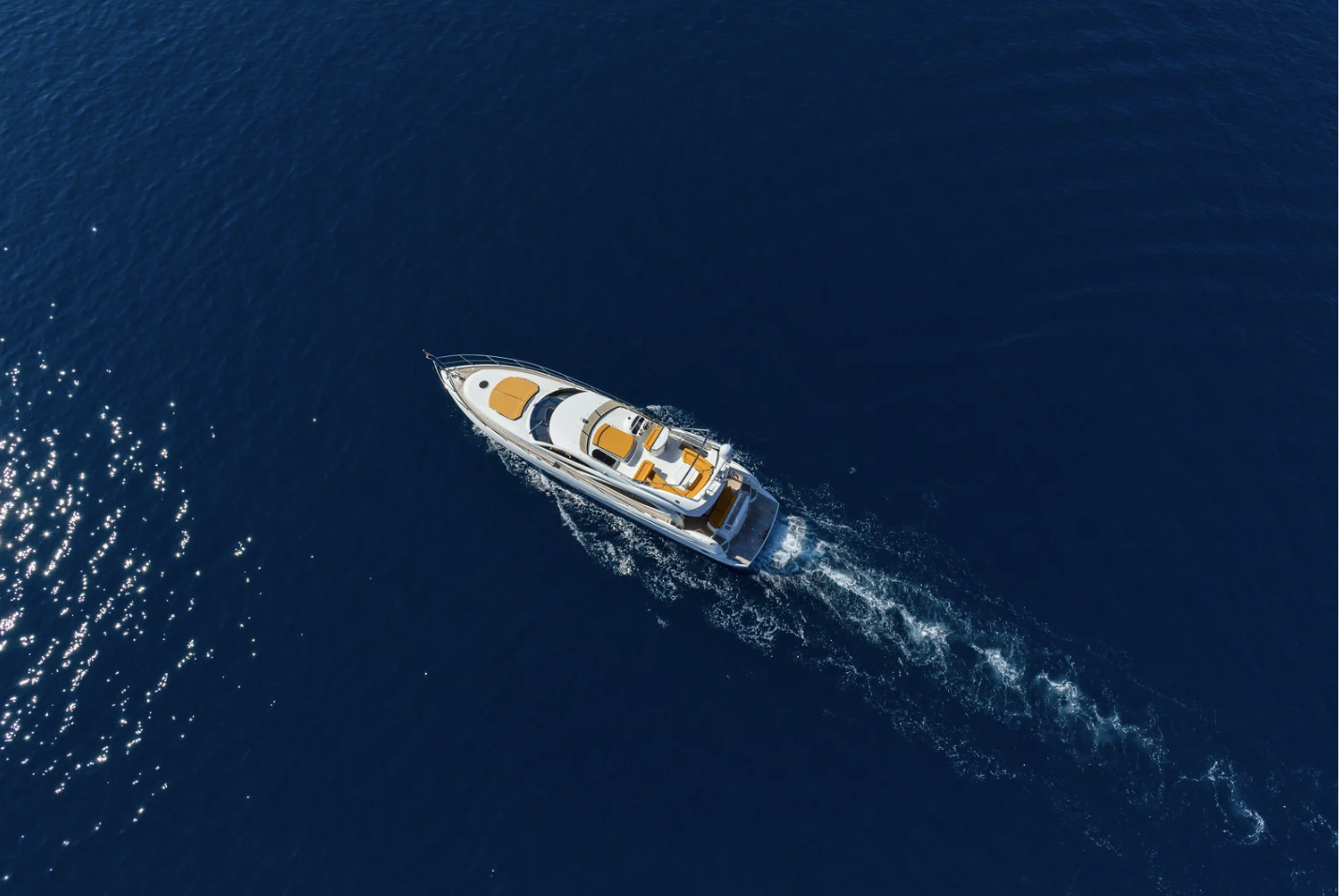 Aerial view of a white yacht with orange accents sailing in the open blue ocean.