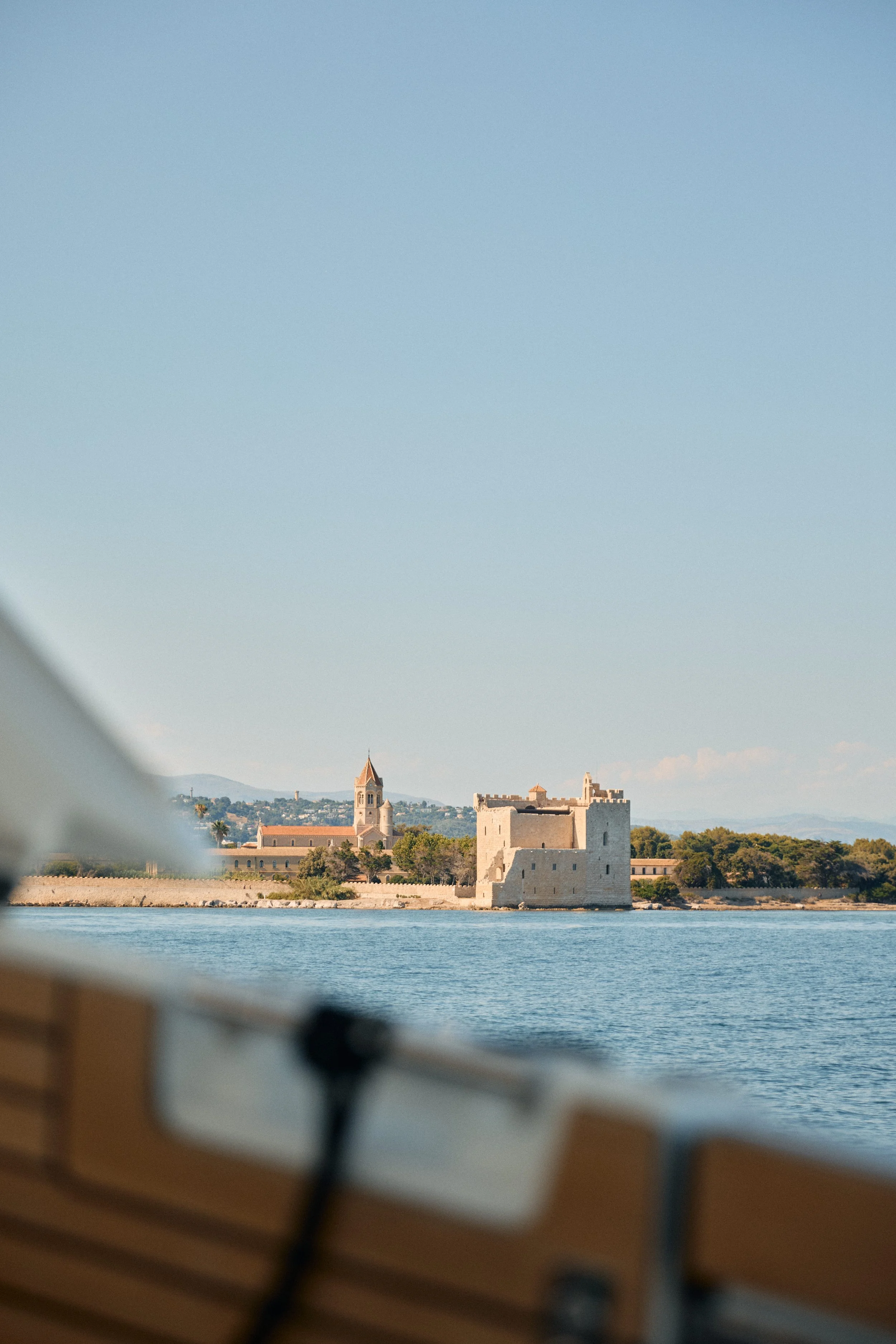 View of a historic castle and church in a coastal town, seen from a boat with part of the boat's interior in the foreground.