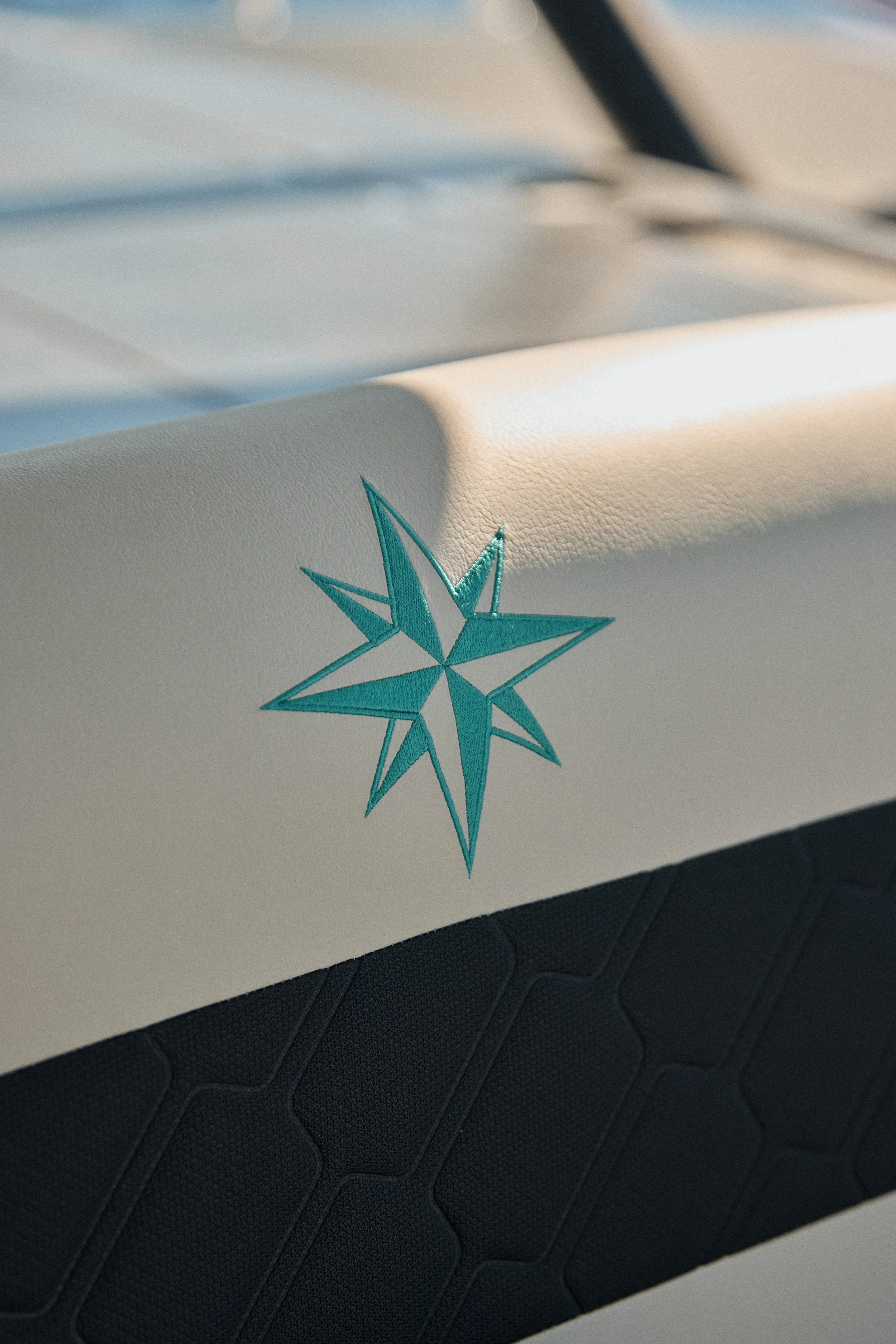 Close-up of a white surface with a teal embroidered star design, possibly part of a bag or fabric, with a textured black background underneath.