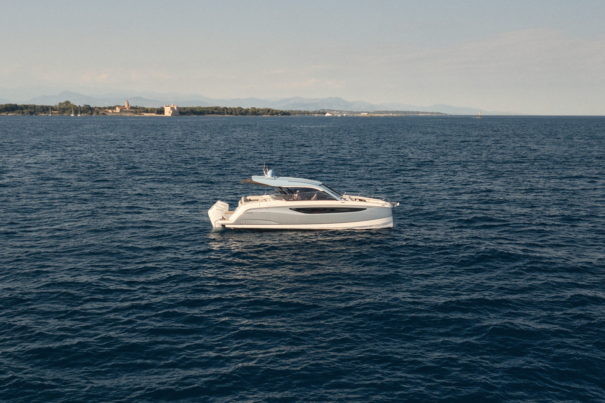 A white motorboat sailing on dark blue ocean water with distant shoreline and mountains in the background.
