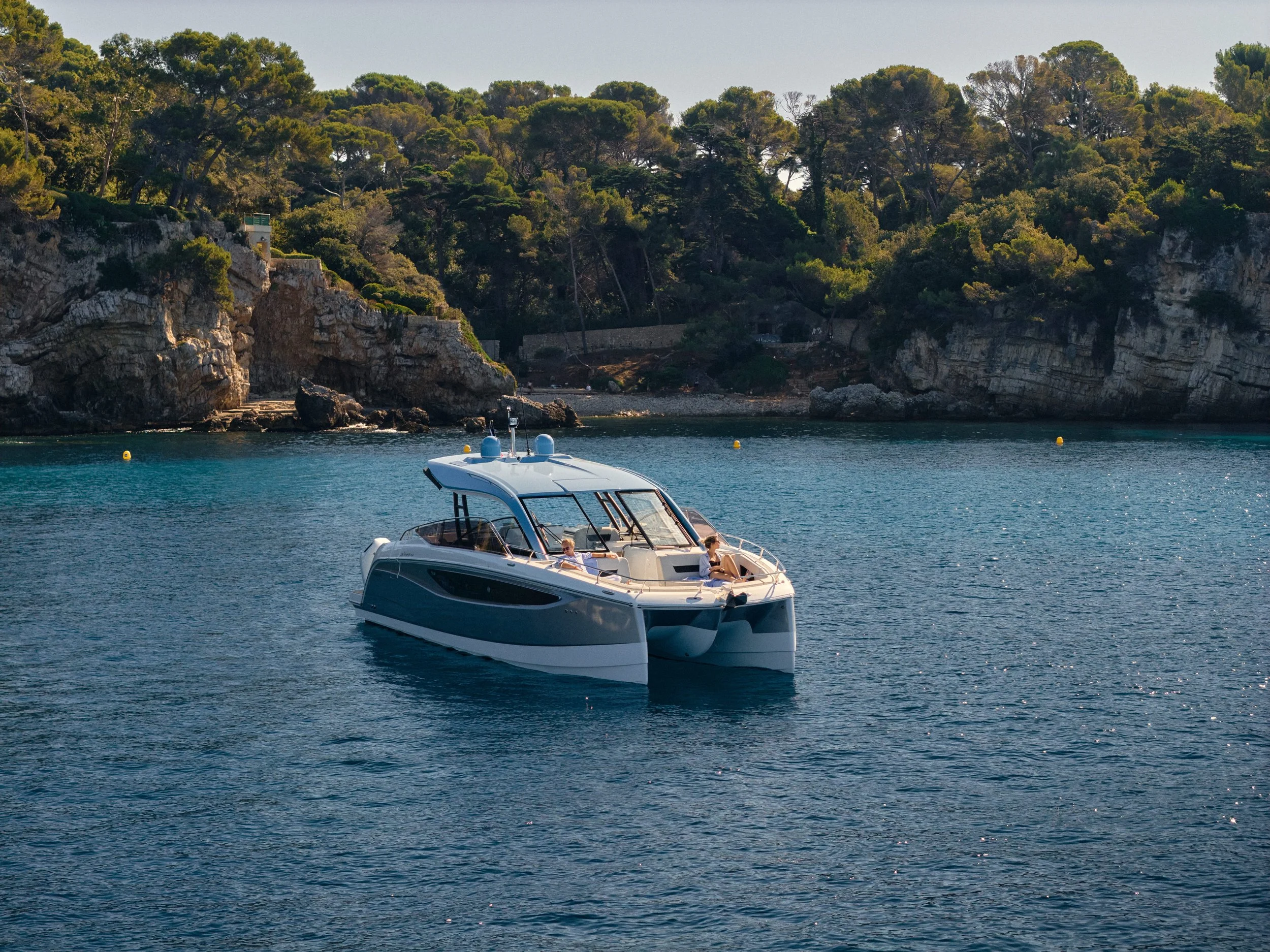 Four people are relaxing on a white yacht, enjoying drinks and playing a board game, on clear blue water.