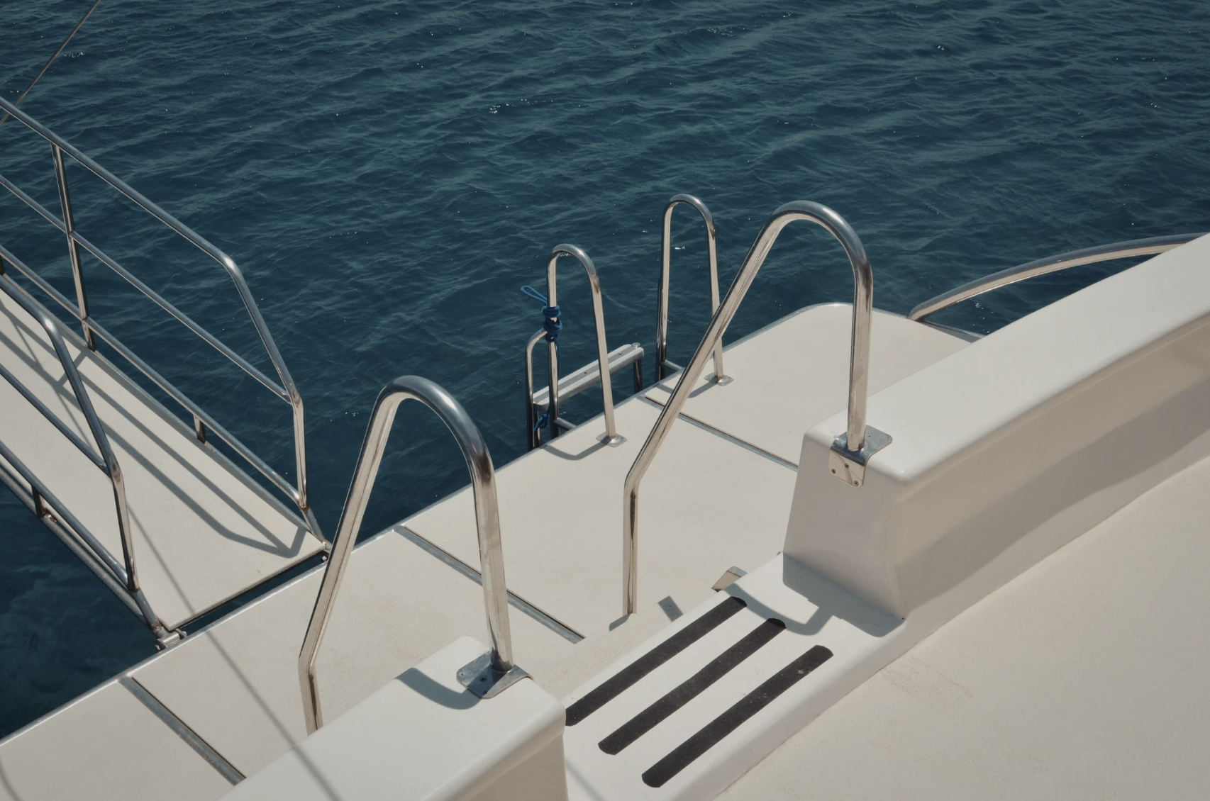View of a boat's deck with metal railings and ladders leading into the water, with open blue ocean surrounding.