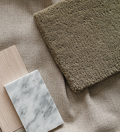 Close-up of a beige textured fabric surface with a folded greenish-brown carpet or rug and two rectangular objects, one with a wooden texture and another with a marble pattern.