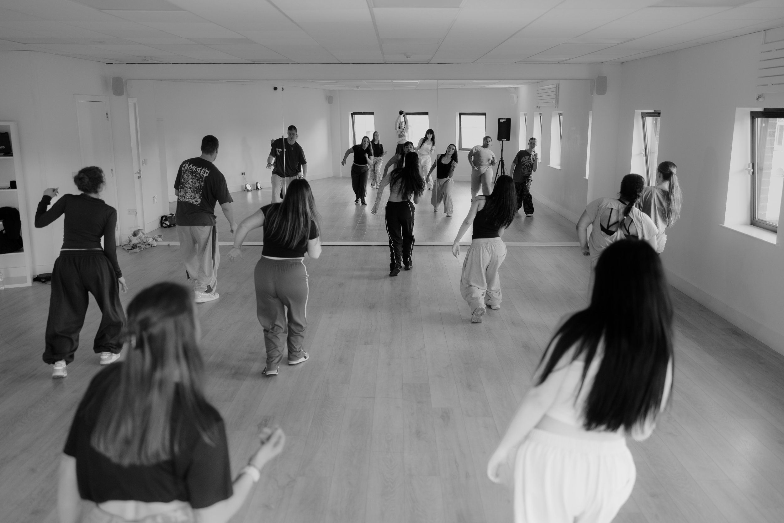 A group of people participating in a dance class in a studio with a large mirror and windows.