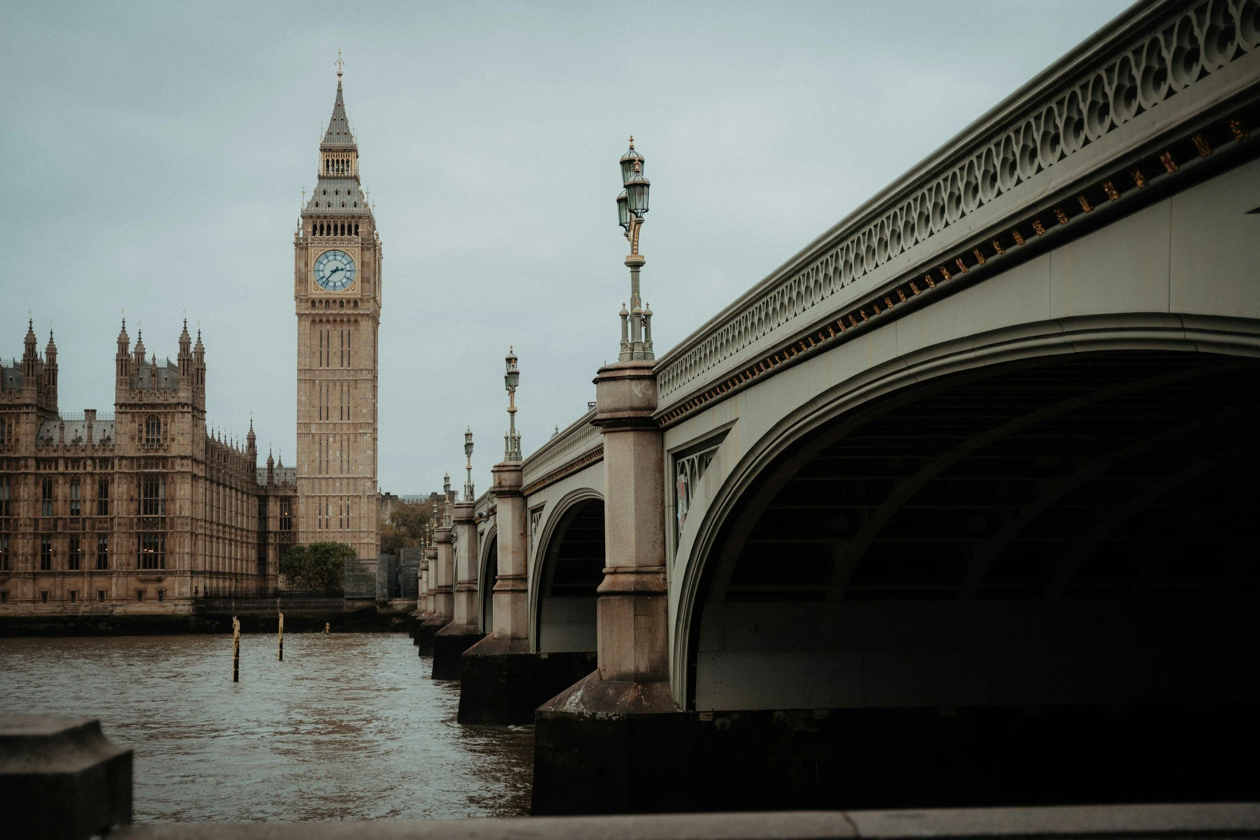 ロンドンのビッグベンとウェストミンスター宮殿が見える風景。川のそばの橋の下から撮影されている。