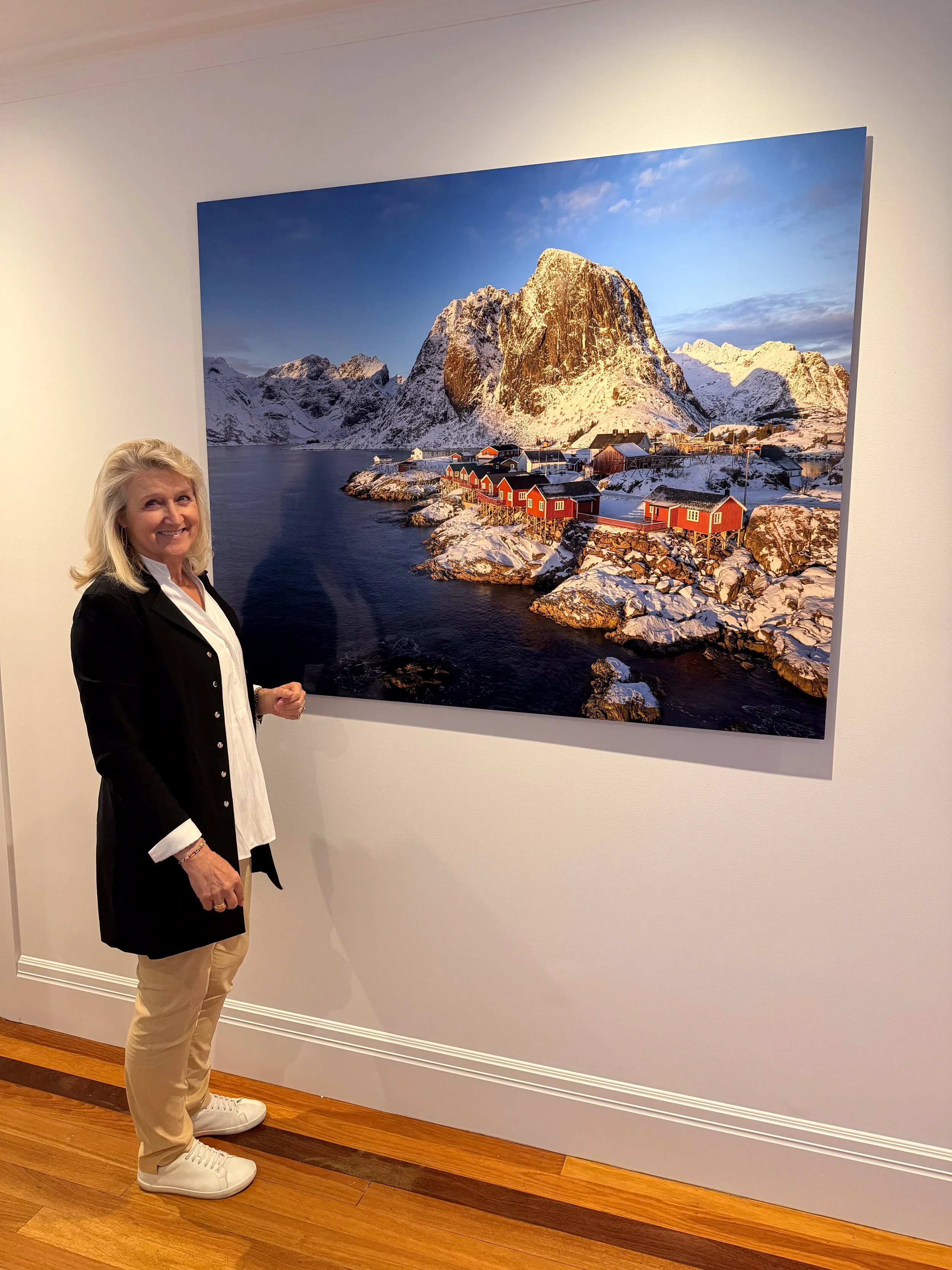 Photographer Linda Berry (Fox) with installed photographic print print of Eliassen Cabins at Hamnoy, Lofoten Islands Norway at a medical centre.