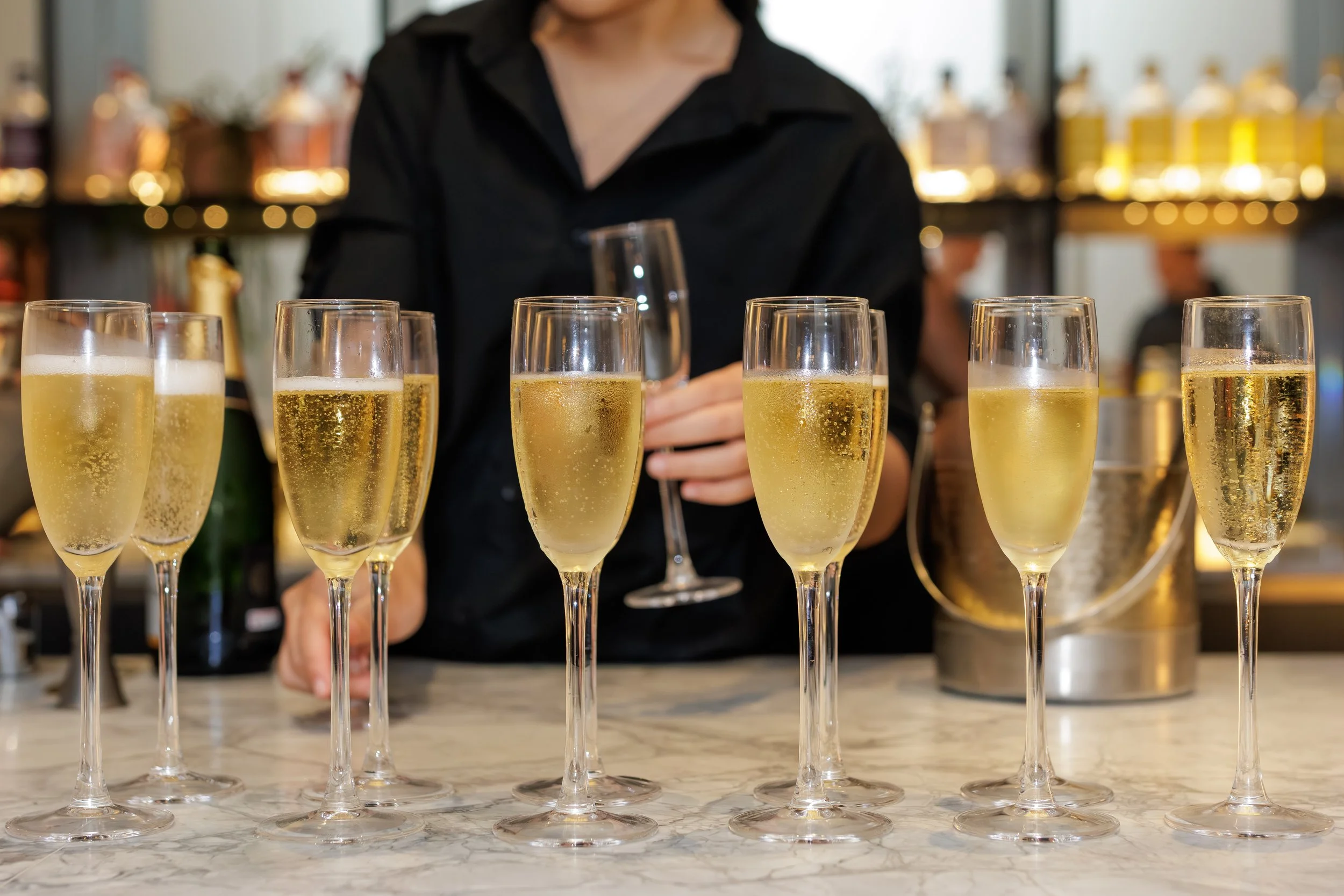 Multiple champagne glasses filled with champagne being served at a bar or restaurant.