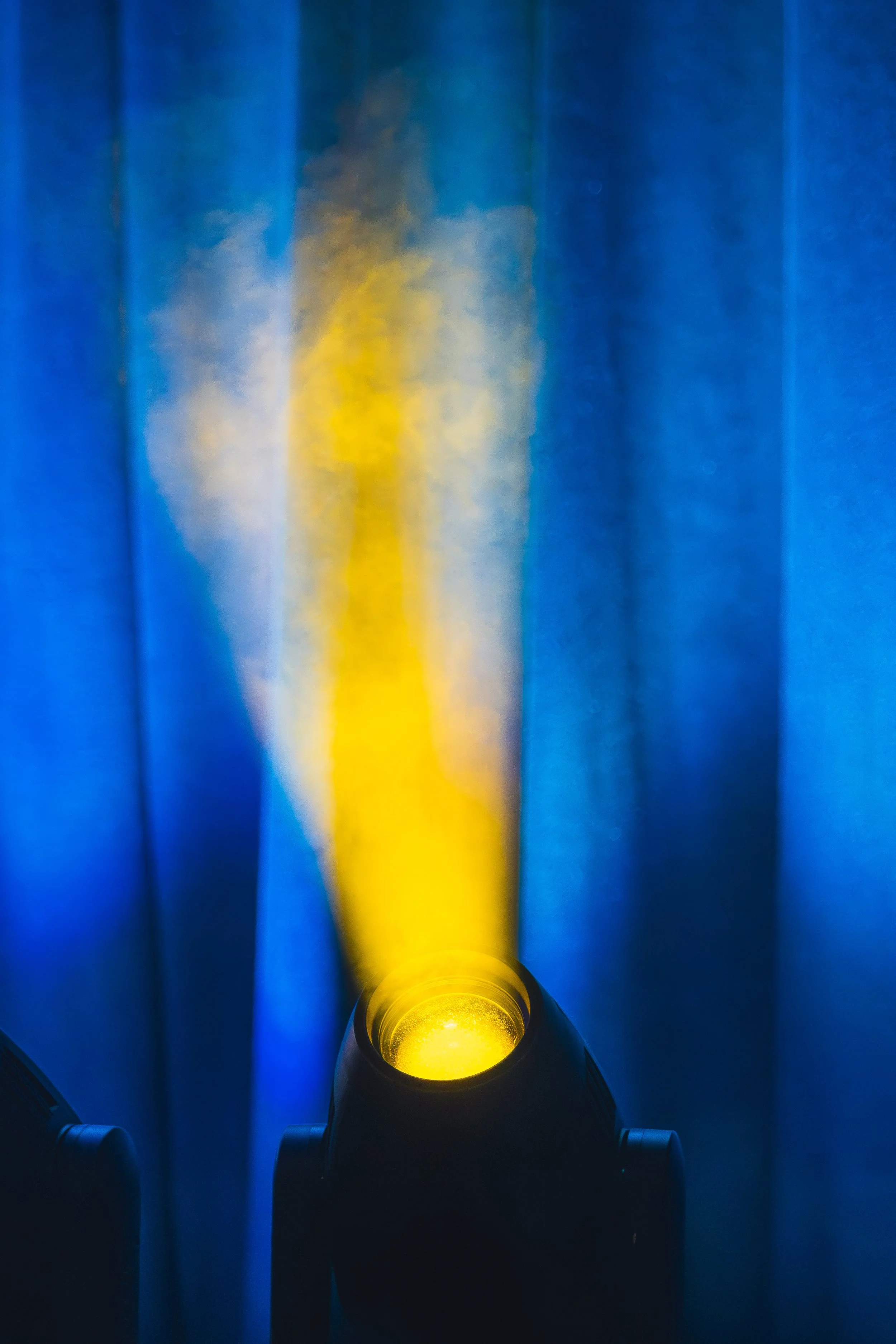 A yellow flashlight shining light through a tube, illuminating the smoke or vapor inside, with blue fabric or curtains in the background.