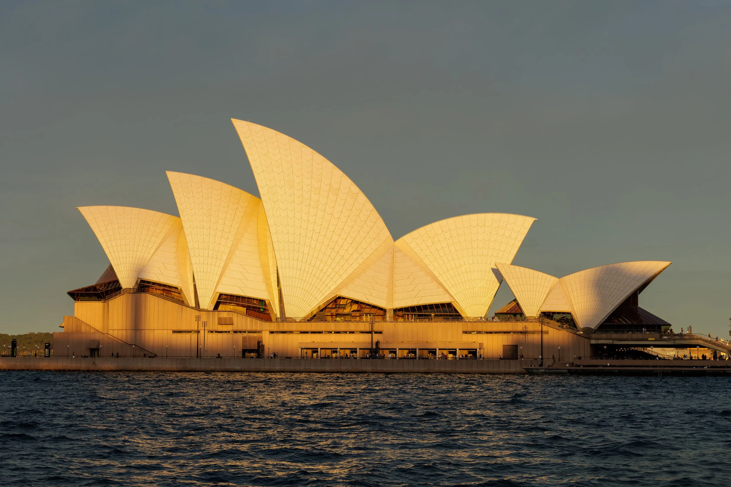 Sydney Opera House illuminated at sunset, with water in foreground and a clear sky.