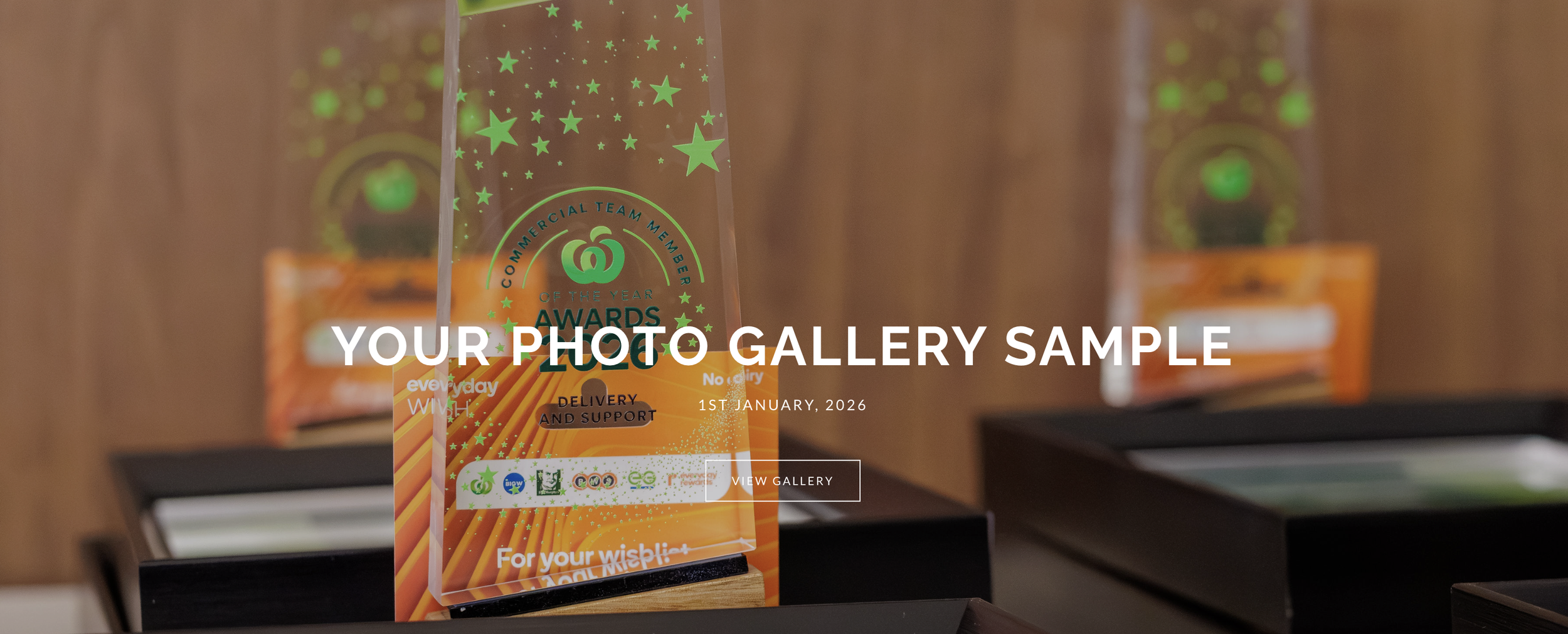 A glass award with green stars and a gold pretzel icon in the center, engraved with text that includes 'Of the Year Awards' and 'Delivery and Support.' The award is displayed on a black stand on a wooden surface, with other awards blurred in the background.