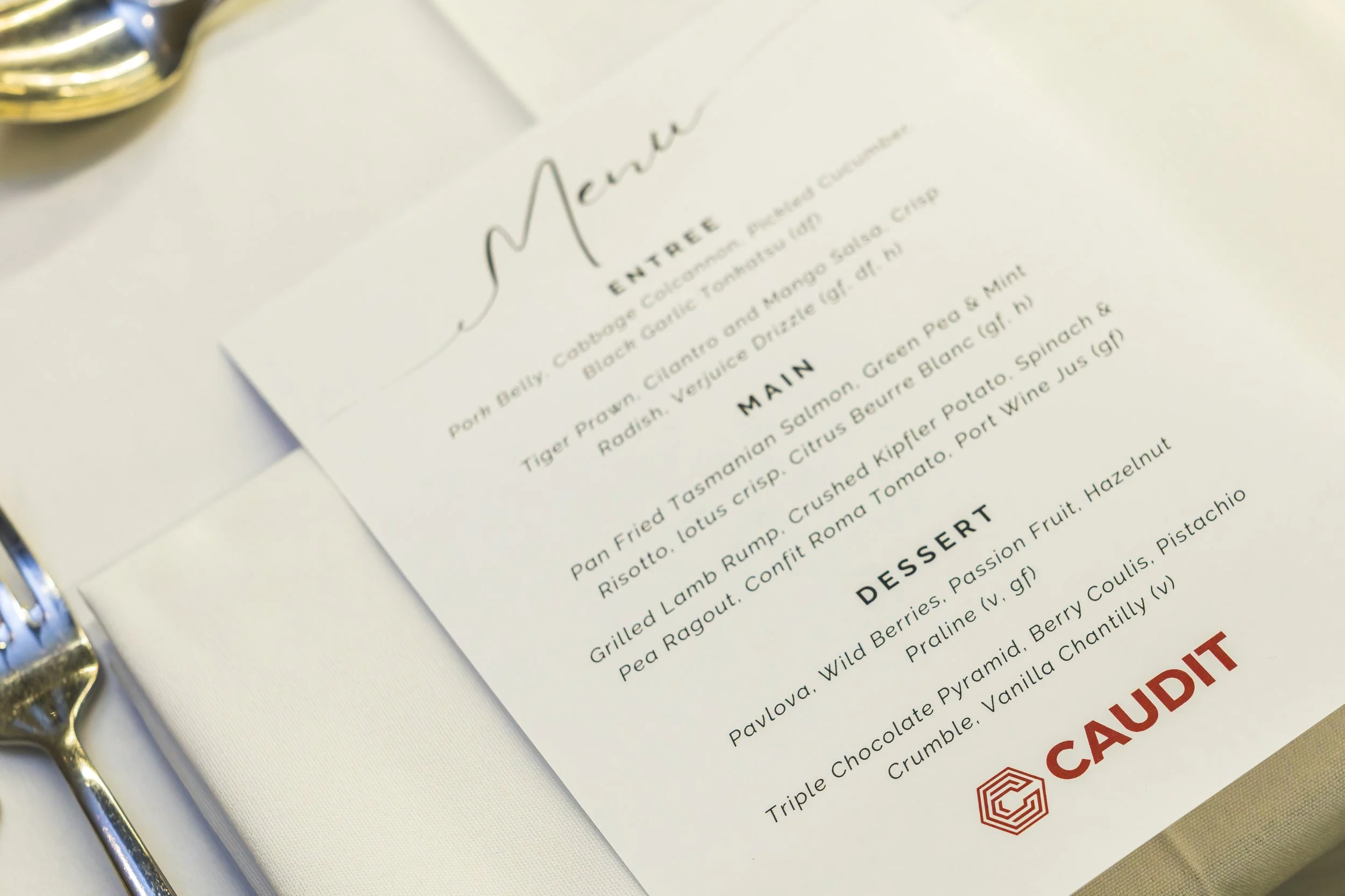 Close-up of a printed restaurant menu on white paper, held open by a metal binder ring, listing appetizers, main courses, and desserts with a focus on the "Entree" section.