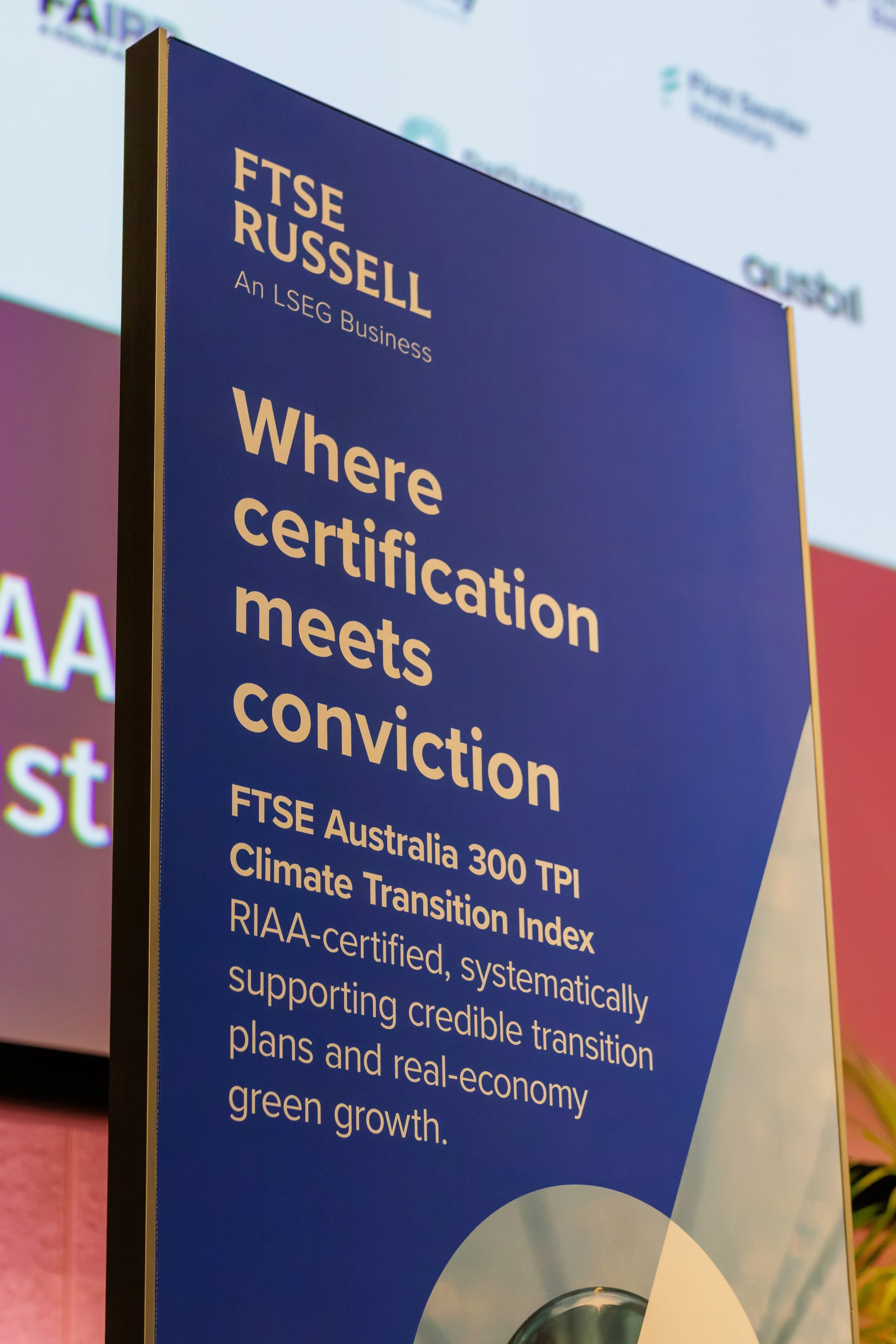 A blue informational poster with white text about FTSE Russell and certification standards, partially visible, with a faint logo in the background.